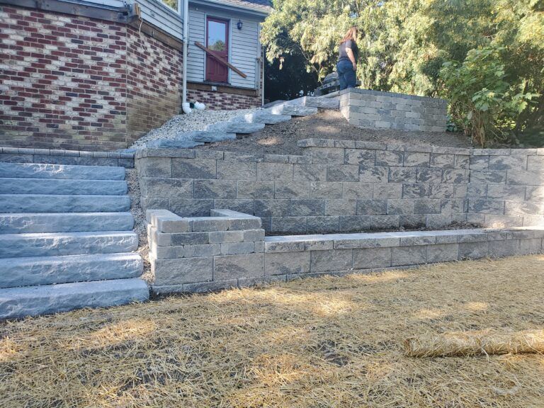 A stone retaining wall with integrated steps and a built-in bench next to a brick house, set against a lawn.