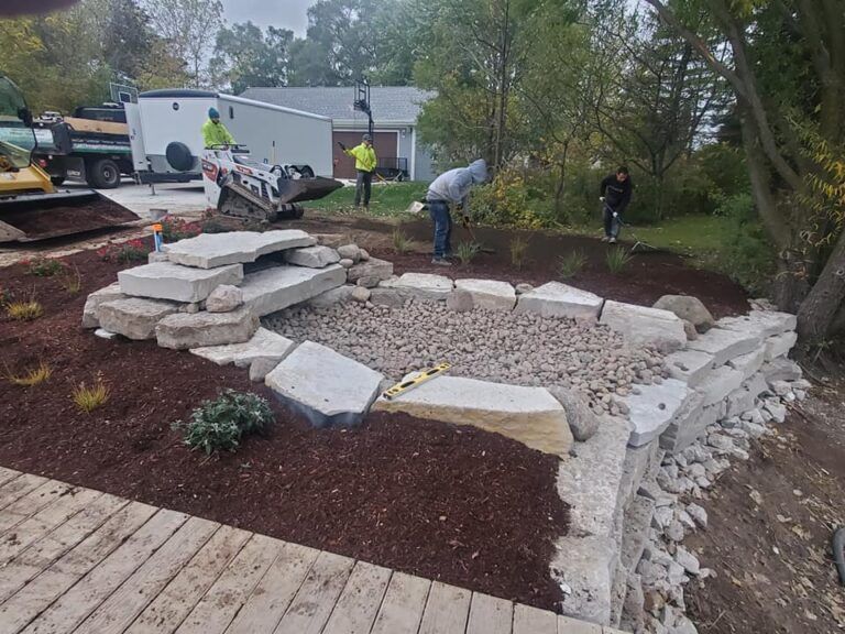Landscapers install a stacked-stone retaining wall and a gravel garden feature in a backyard setting.