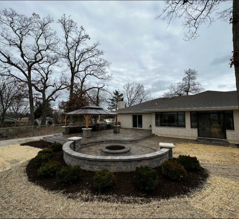 A backyard patio featuring a curved stone fire pit, a gazebo, and fresh landscaping on a cloudy day.