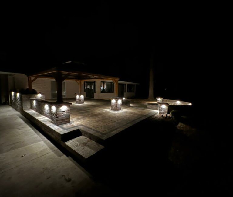 A stone patio with a gazebo, illuminated at night by warm-toned lights built into the walls and pillars.