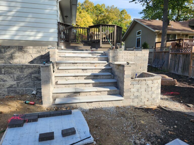 A set of stone steps leading to a wooden deck next to a house with siding, under construction in a yard.
