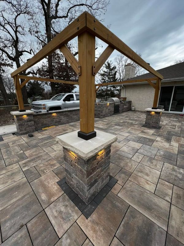 Outdoor patio featuring a wooden pergola structure supported by stone pillars with integrated warm accent lighting.