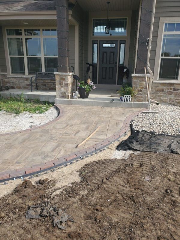 A new stamped concrete walkway leads to the front door of a suburban house, with surrounding landscaping still in progress.