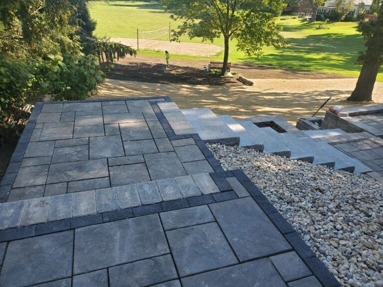 Gray stone patio and steps overlooking a backyard lawn with a volleyball net.