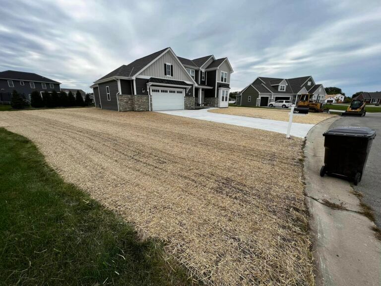 A new, two-story house with a white driveway and freshly laid, straw-covered sod in the front yard on a cloudy day.
