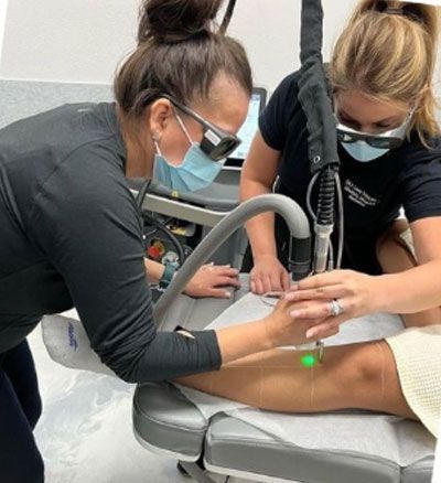 Two women wearing masks are working on a patient's leg.