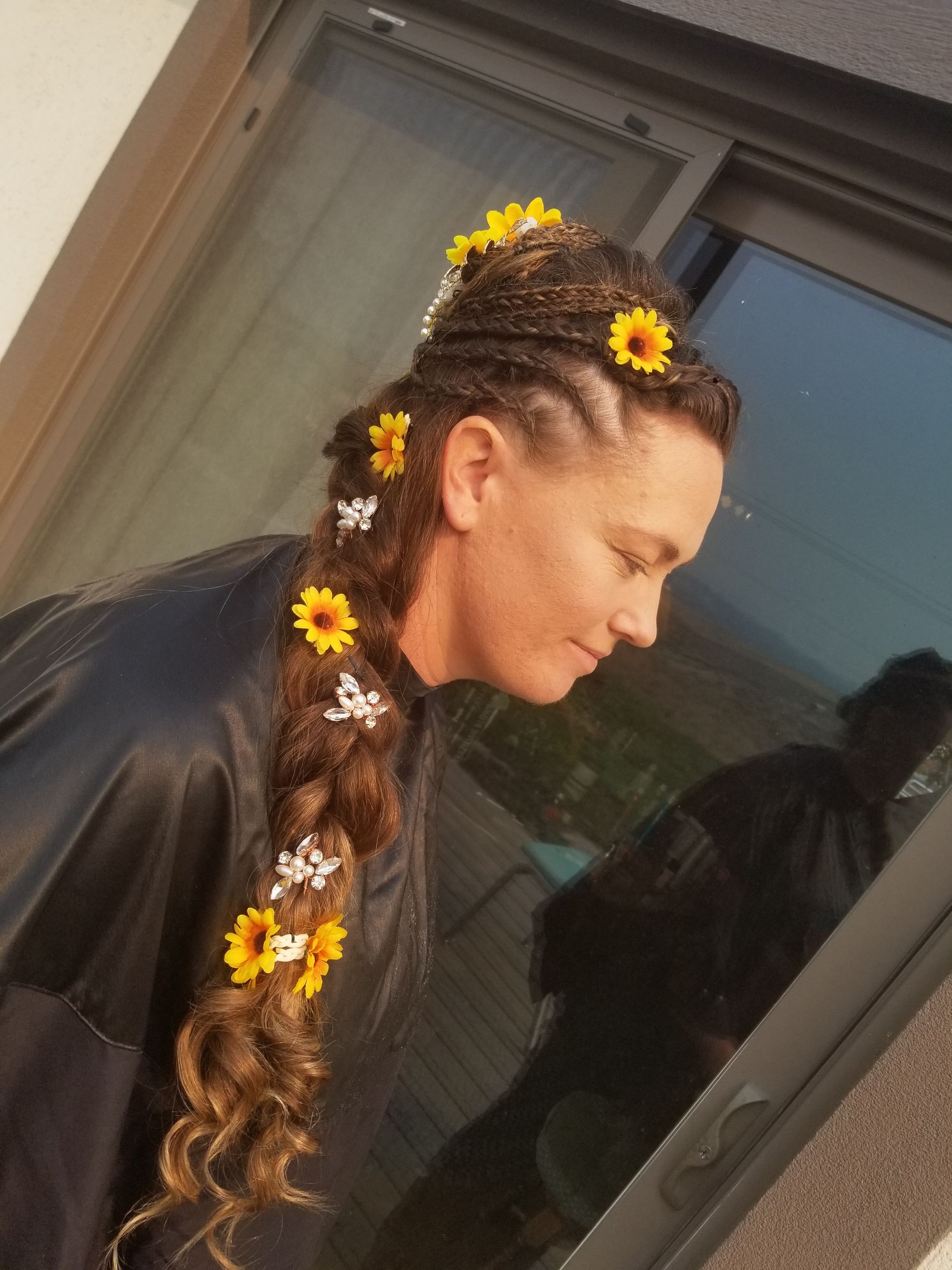 A woman with flowers in her hair is standing in front of a window.