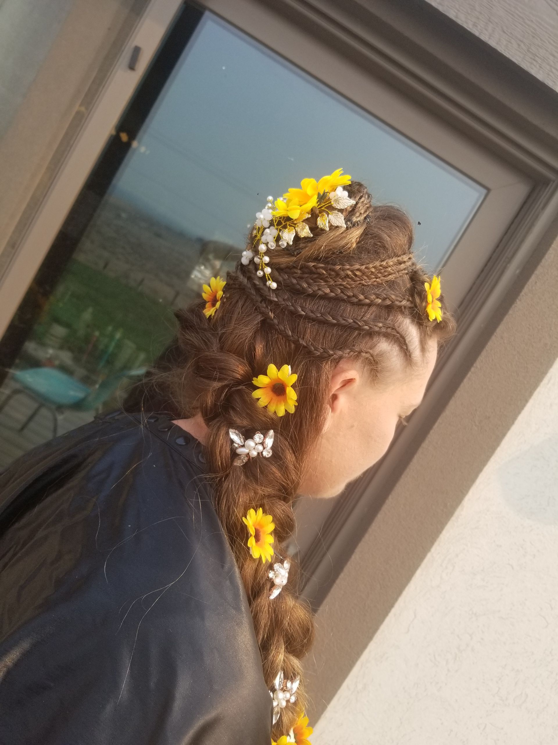 A woman with flowers in her hair is standing in front of a window.