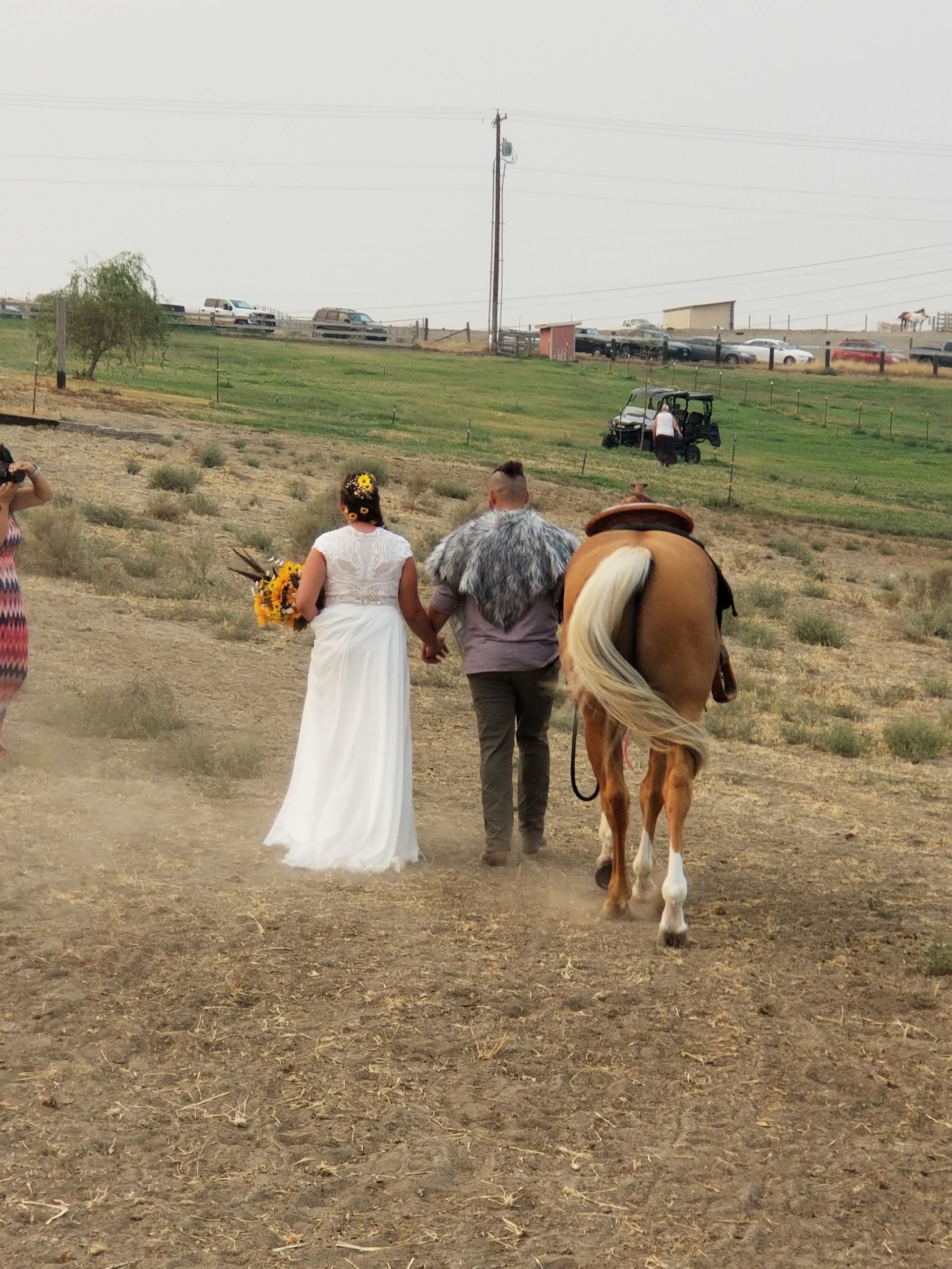 A bride and groom walking with a horse in a field