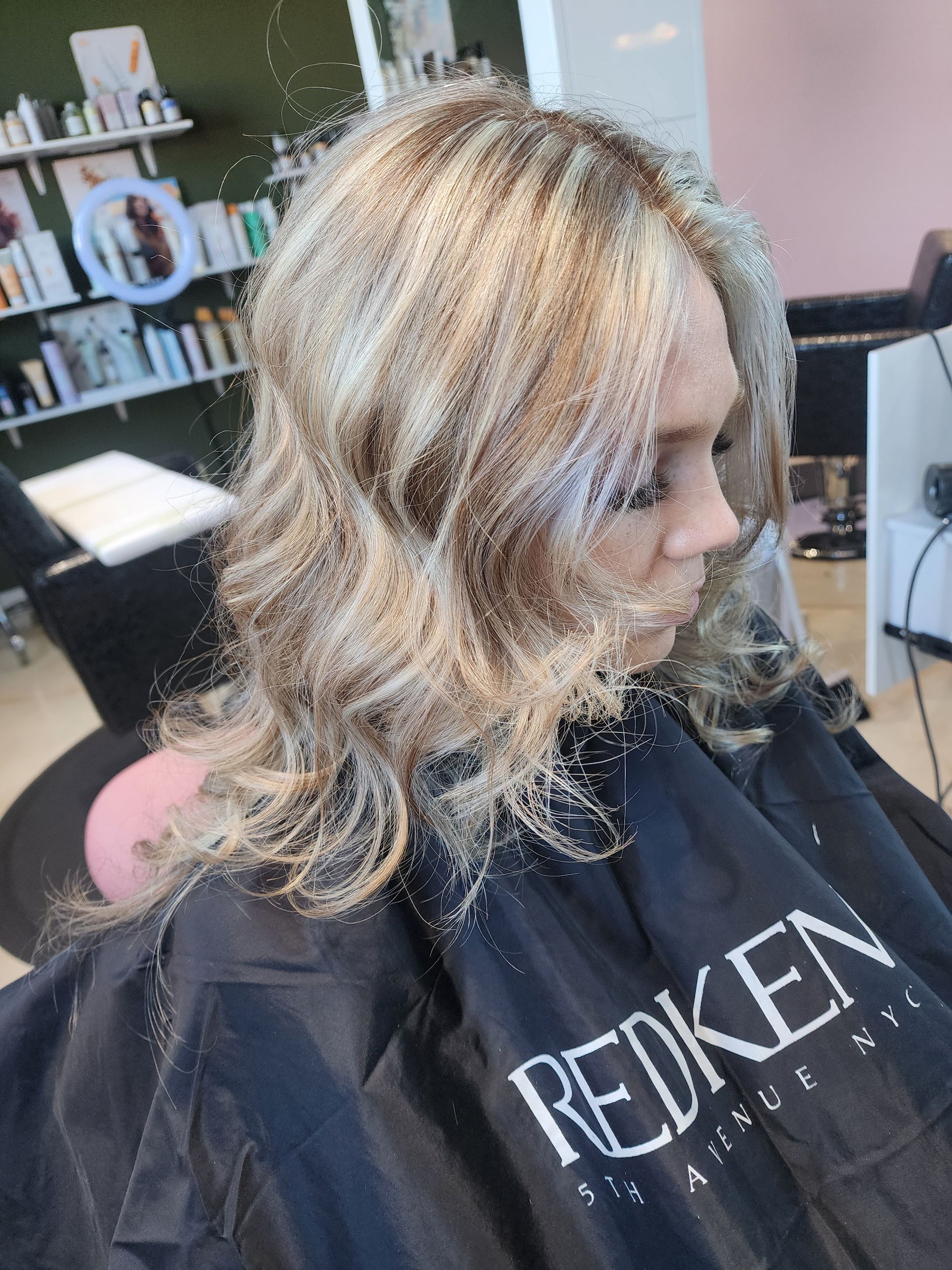 A woman is getting her hair cut in a salon while wearing a redken cape.