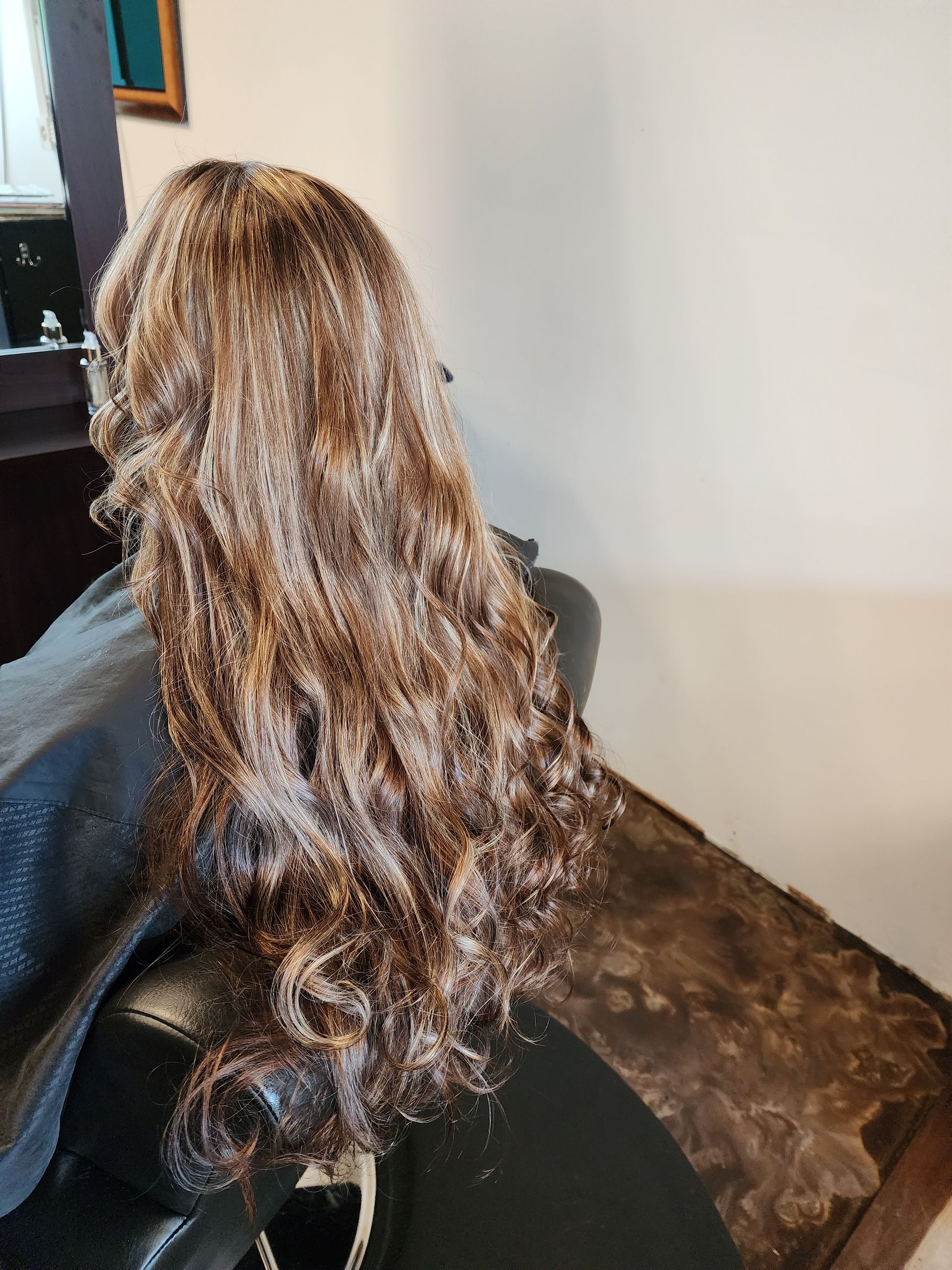 A woman with long curly hair is sitting in a chair in a salon.