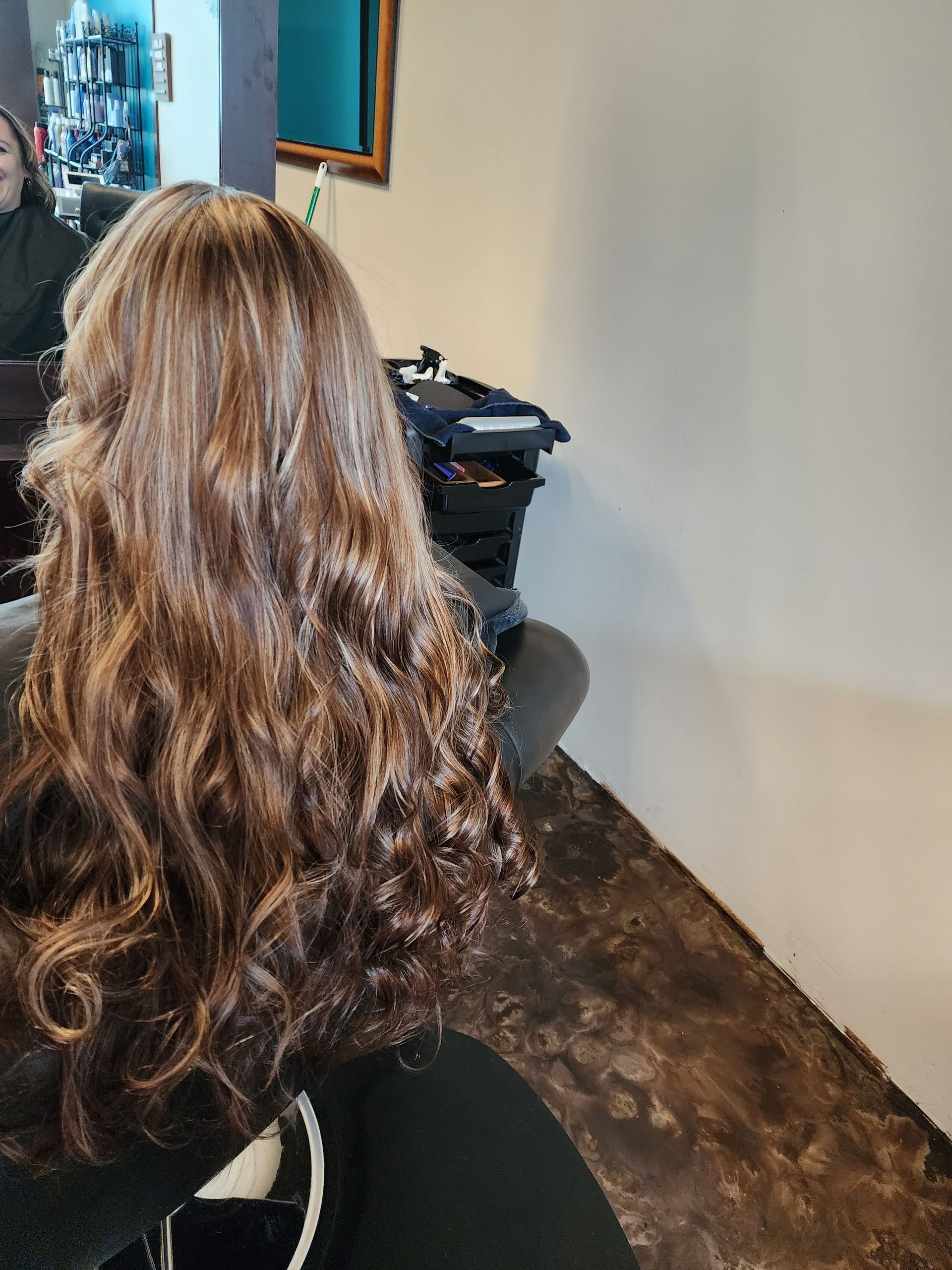 A woman with long brown hair is sitting in a chair in a salon.