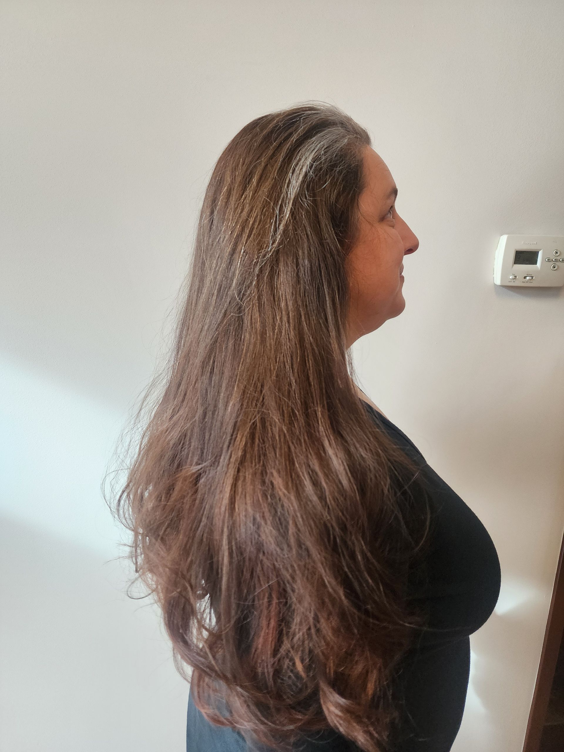A woman with long brown hair is standing in front of a white wall.