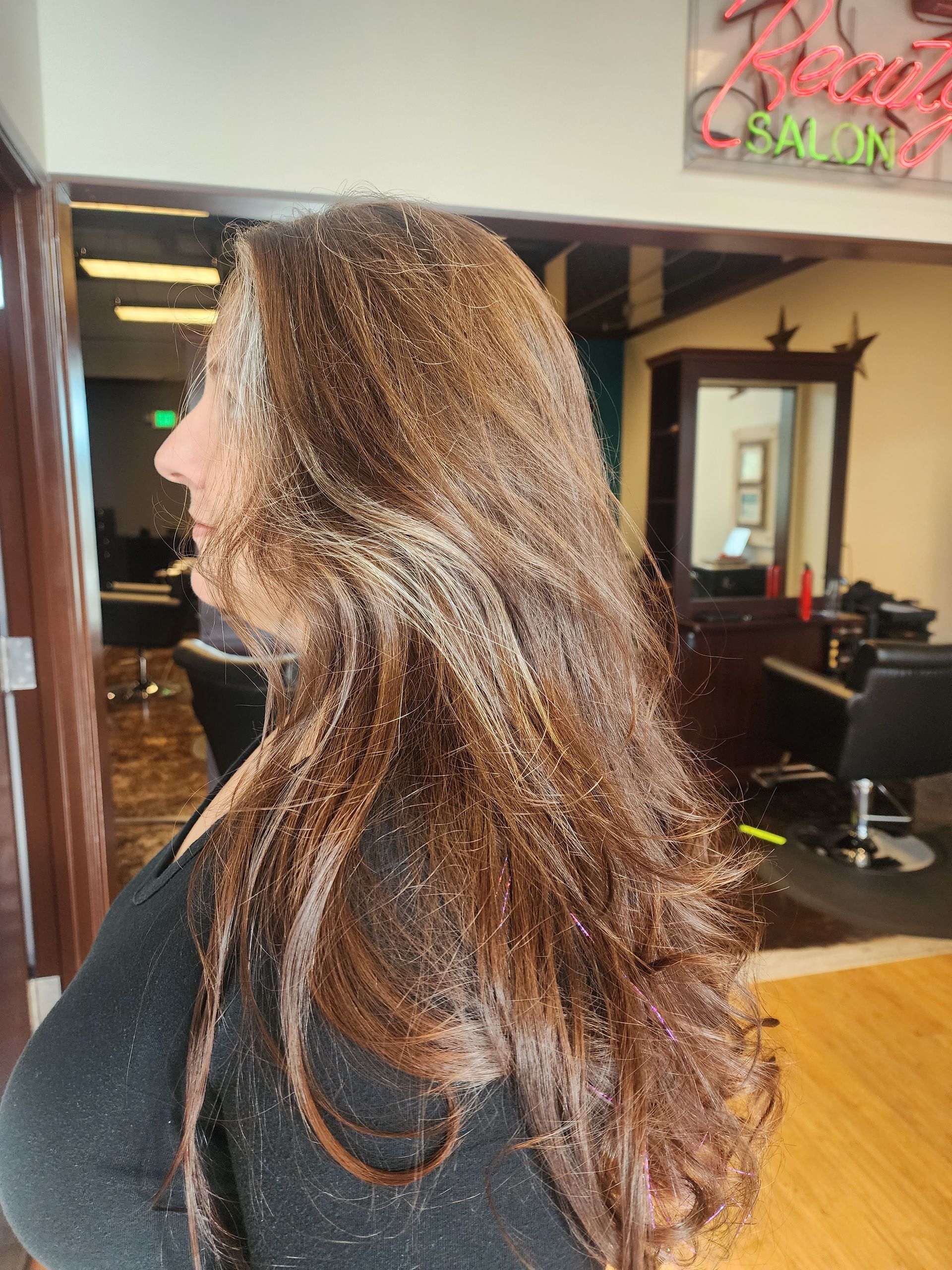 A woman with long brown hair is standing in a salon.