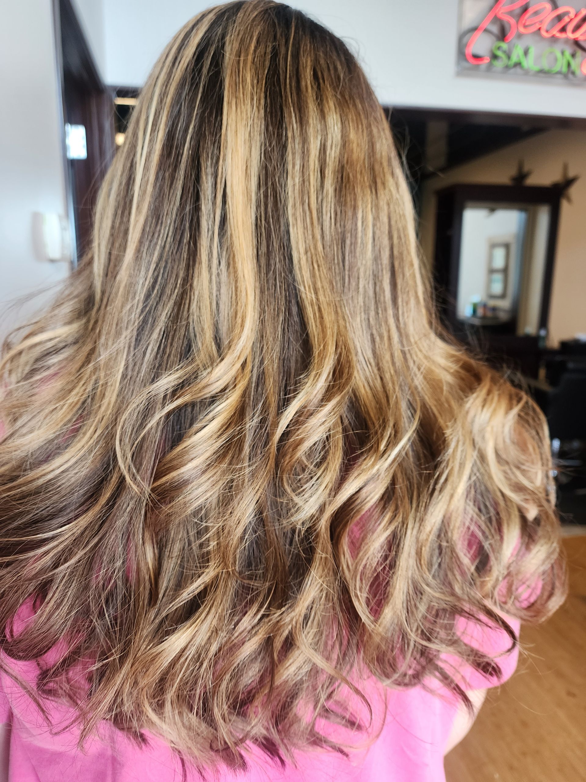 A woman with long wavy hair is wearing a pink shirt.
