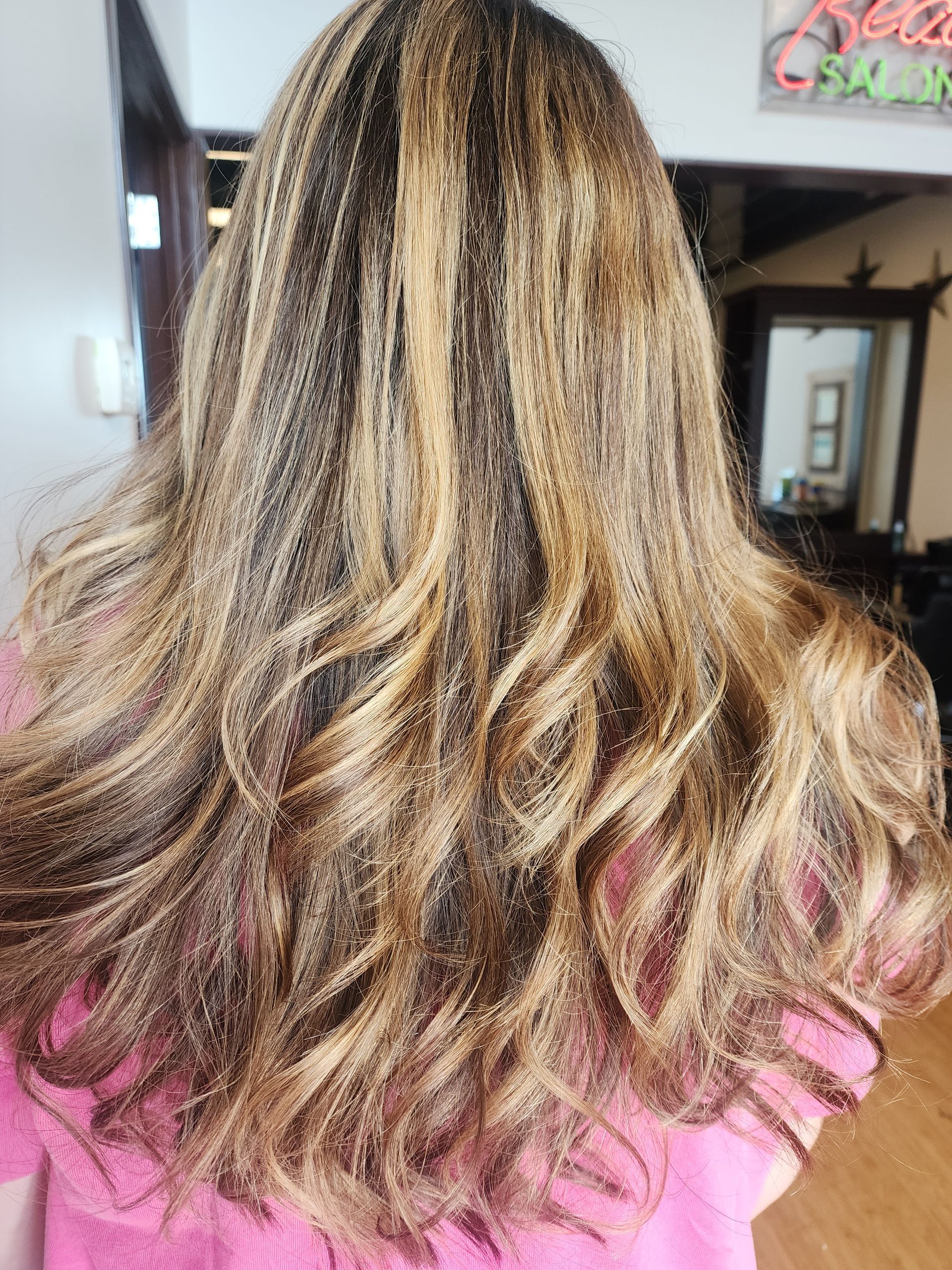 A woman with long blonde hair is wearing a pink shirt.