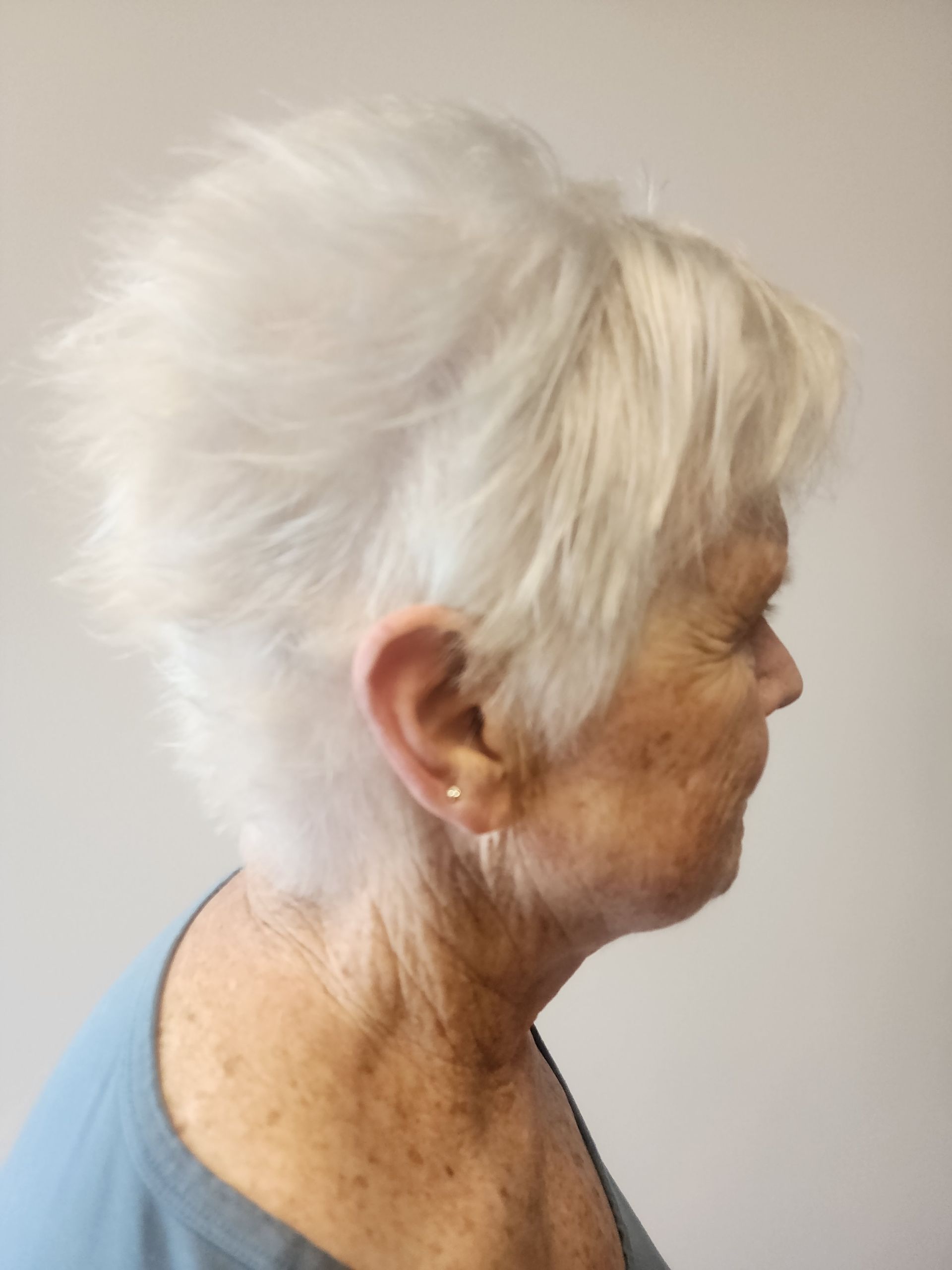 A woman with short white hair is wearing a blue shirt and earrings.