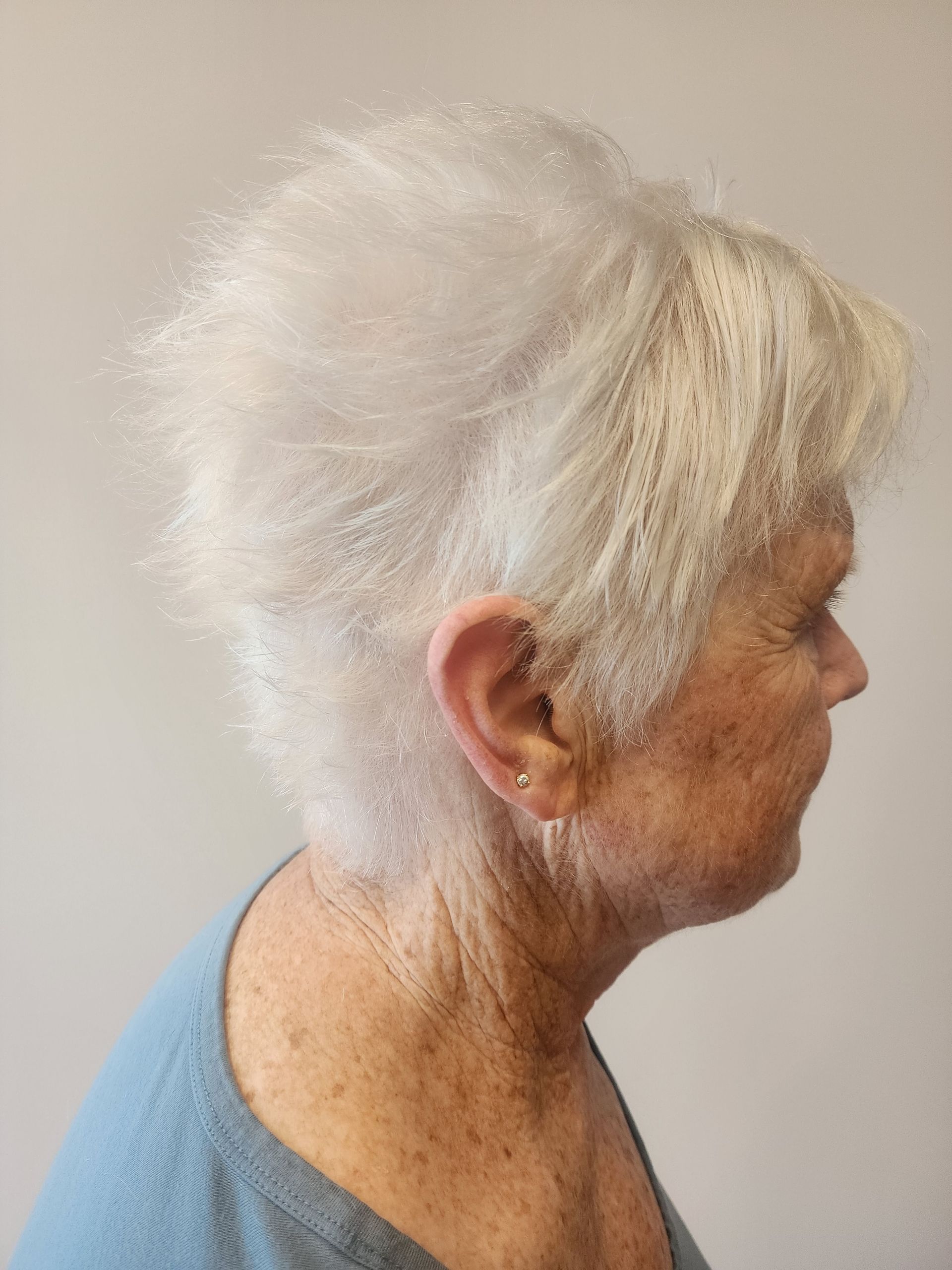 A woman with white hair is wearing a blue shirt and earrings.