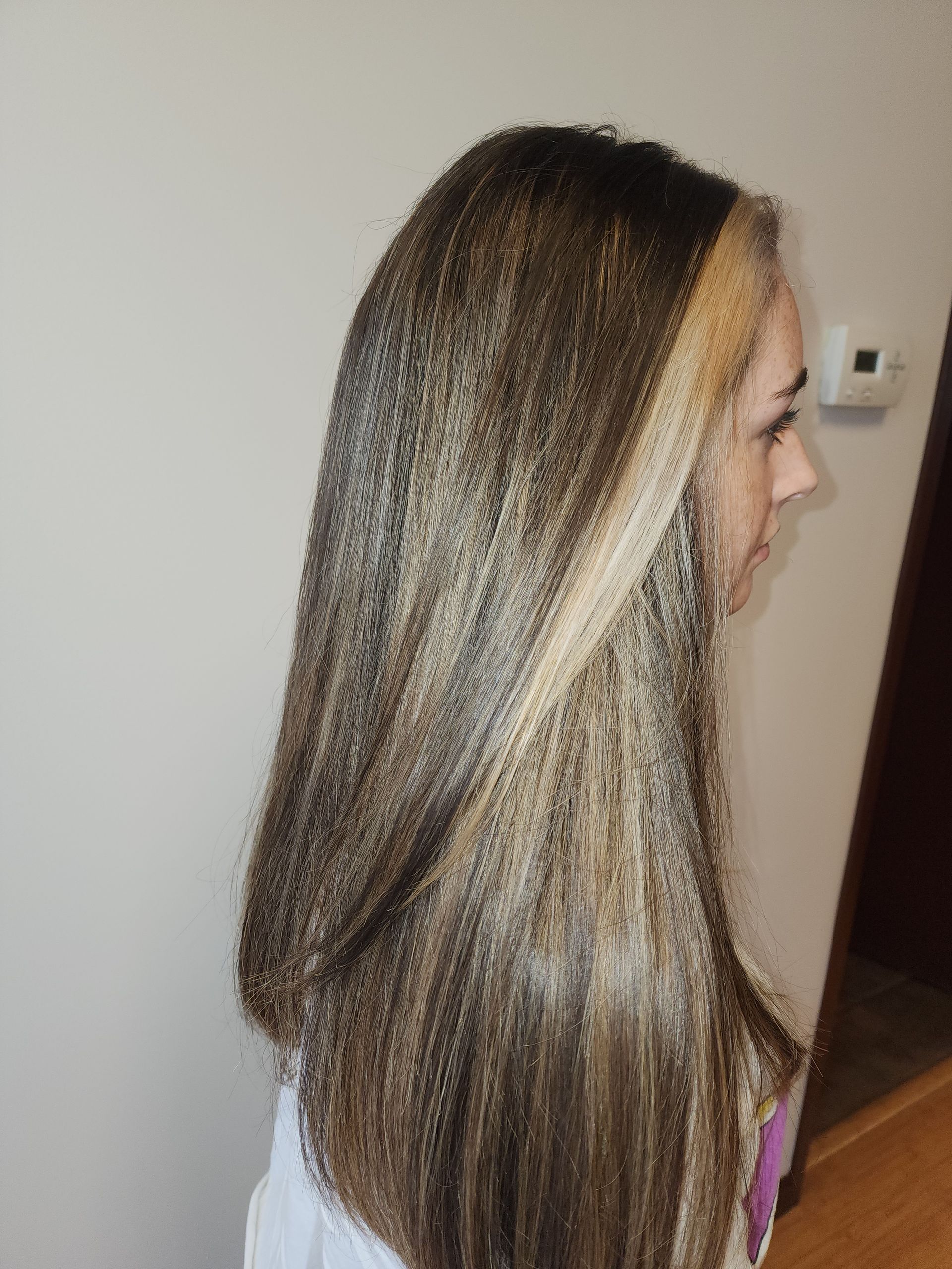 A woman with long brown hair and blonde highlights is standing in a room.
