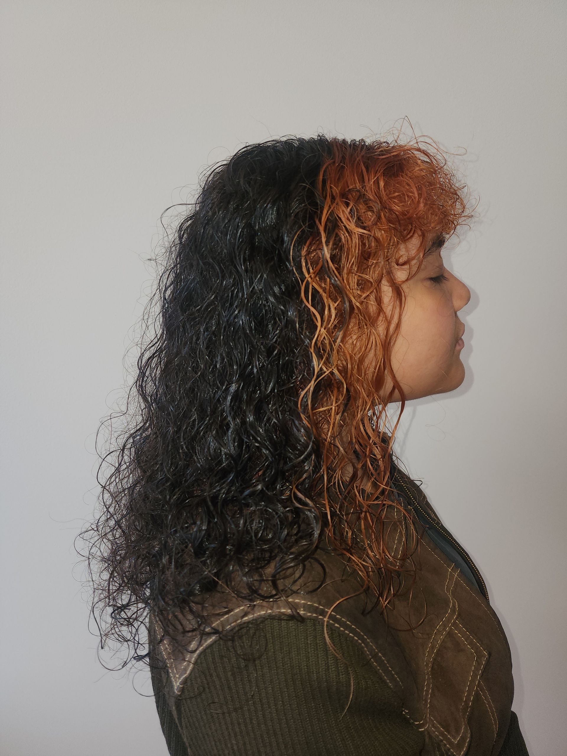 A woman with curly hair is standing in front of a white wall.