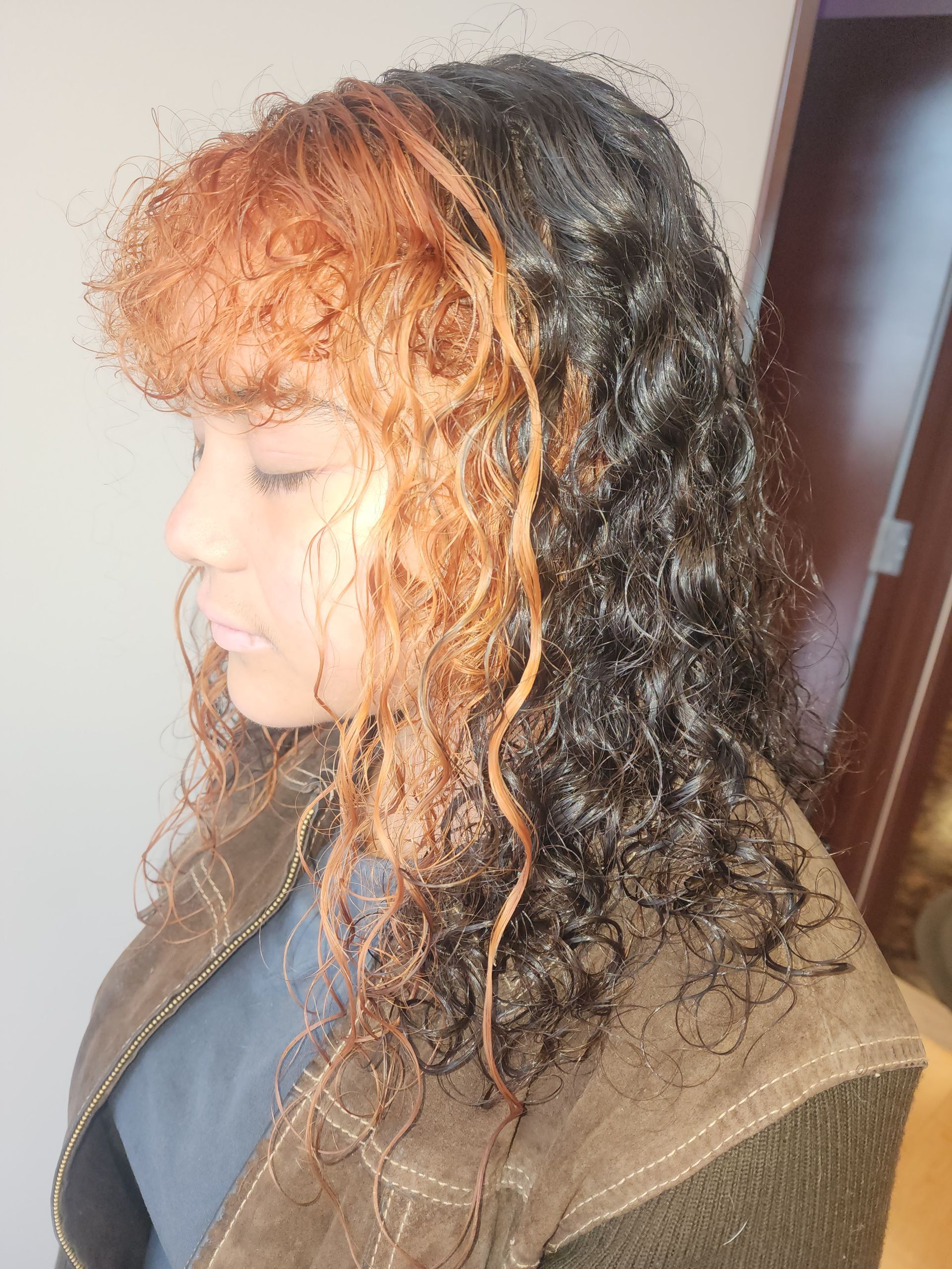 A woman with curly hair is wearing a brown jacket.