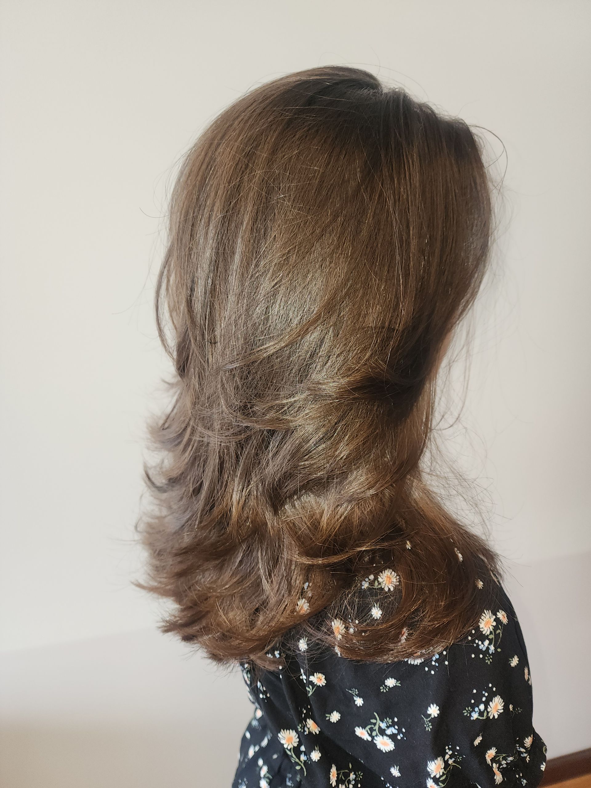 A woman with long brown hair is wearing a floral dress.