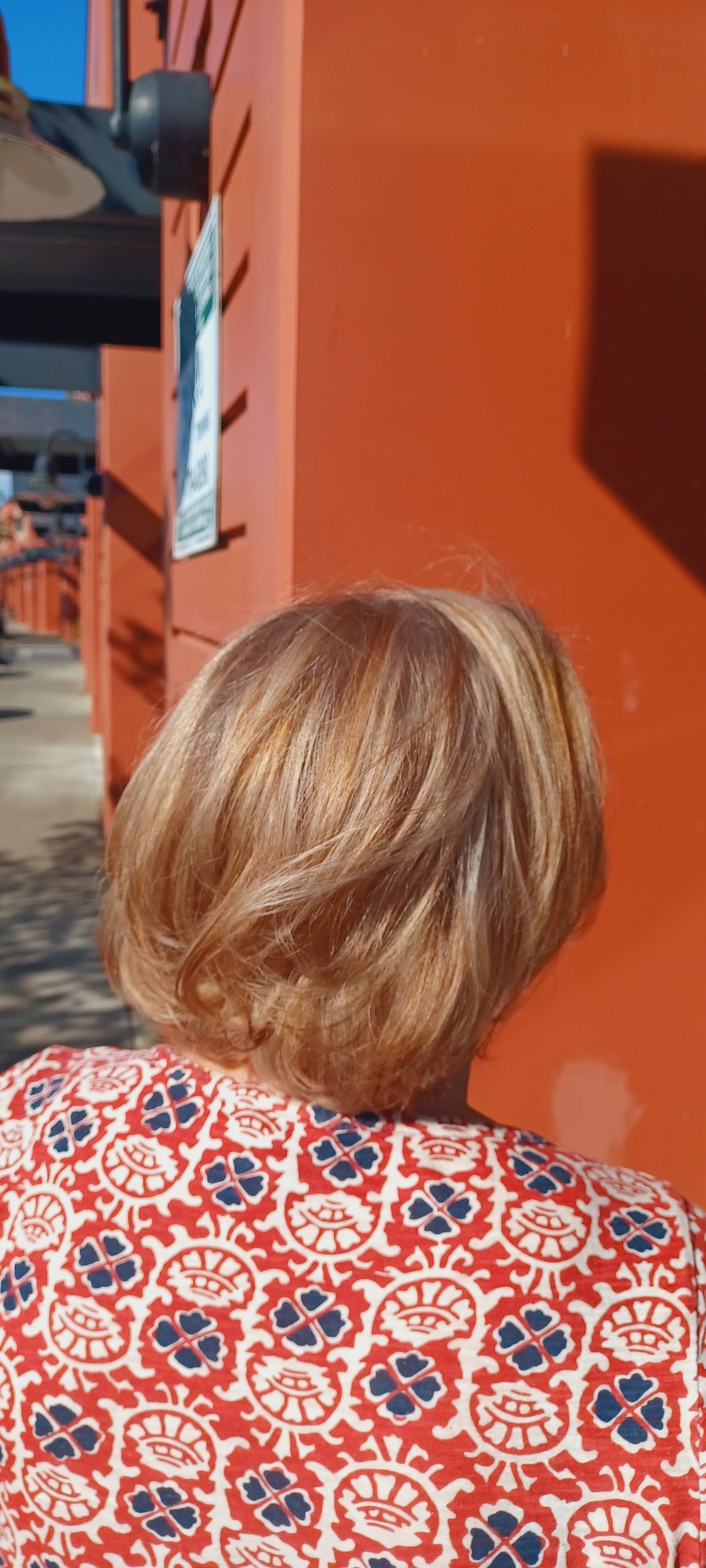 A woman with blonde hair is standing in front of a red building.