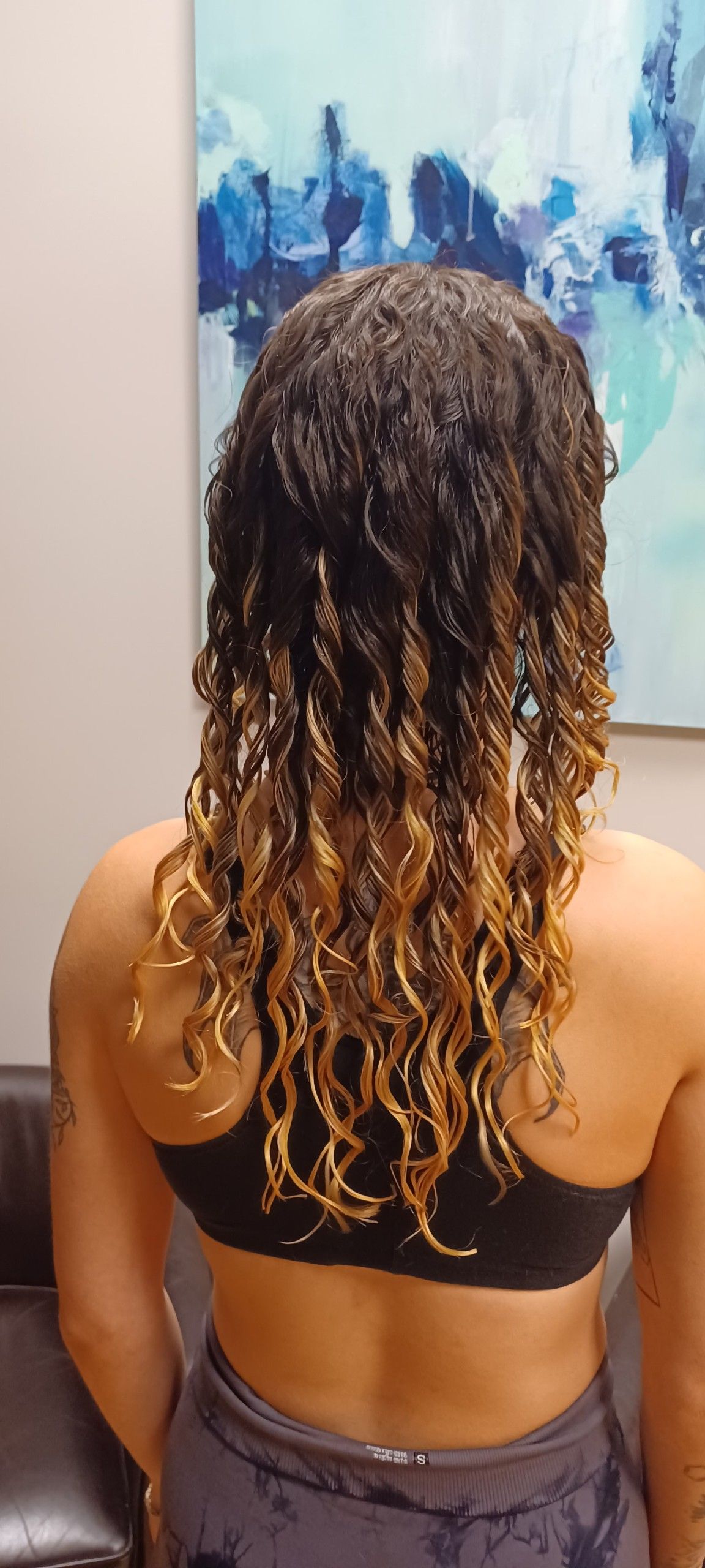 A woman with curly hair is sitting in a chair in front of a painting.