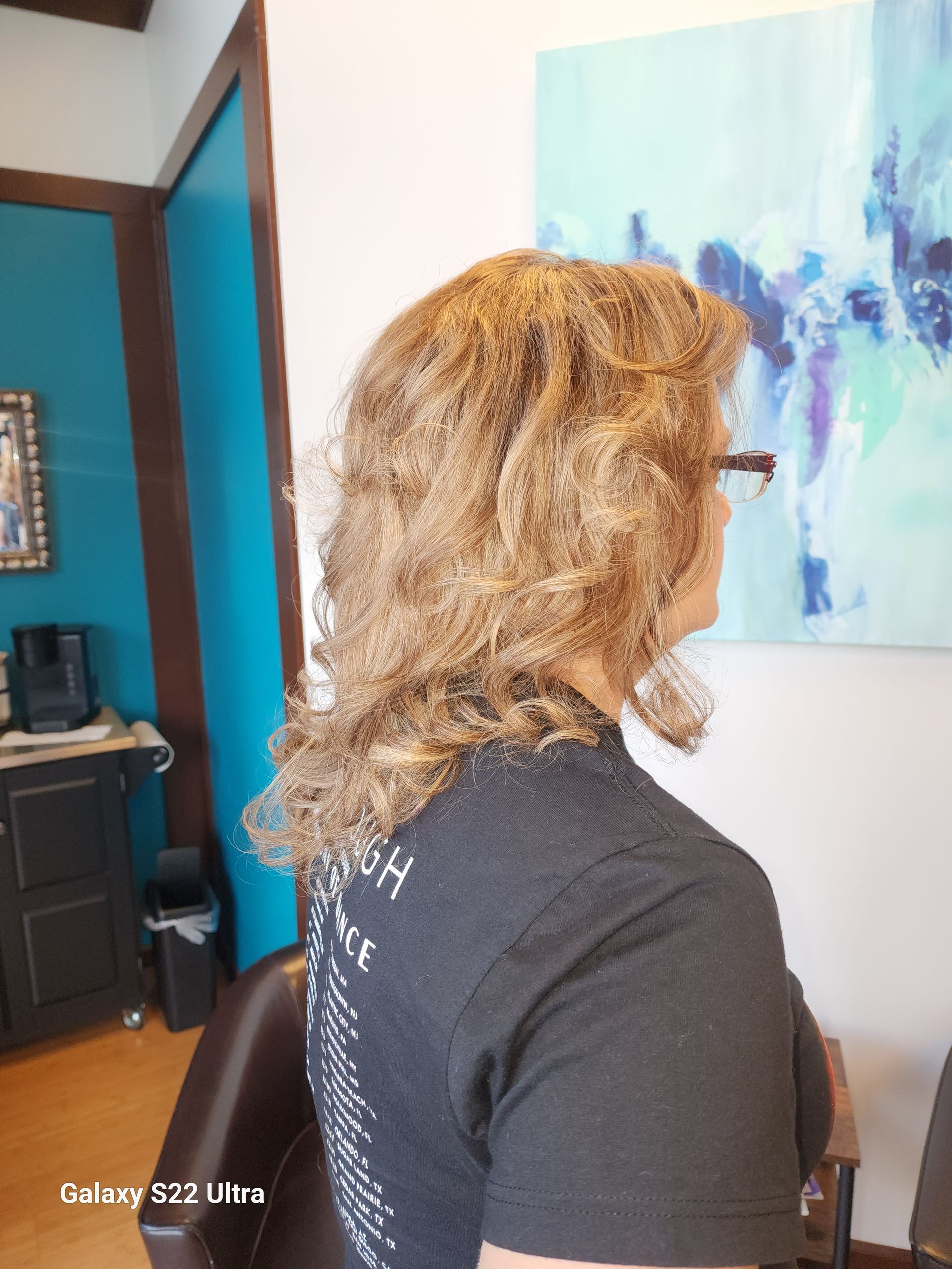 A woman with long curly hair is sitting in a chair in front of a painting.