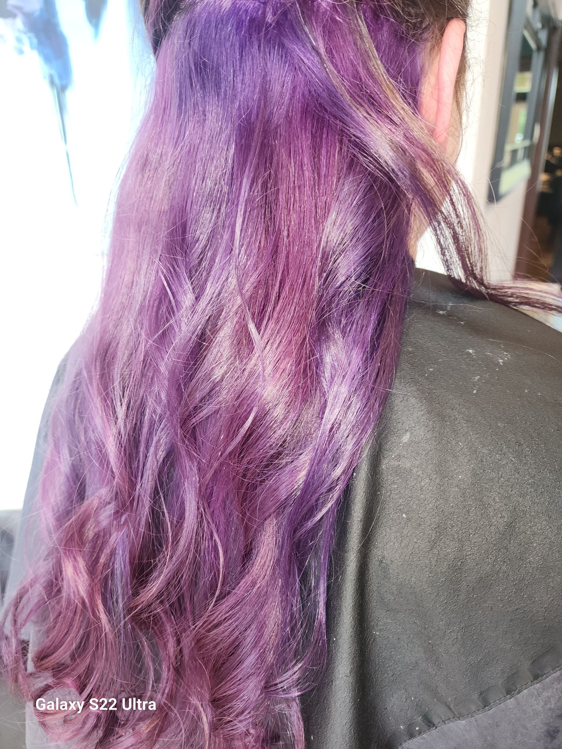 A woman with purple hair is wearing a black cape.