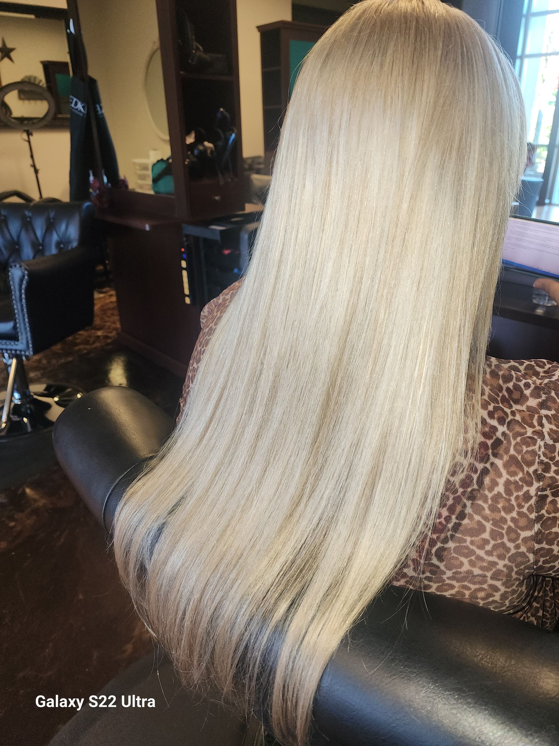 A woman with long blonde hair is sitting on a couch in a salon.