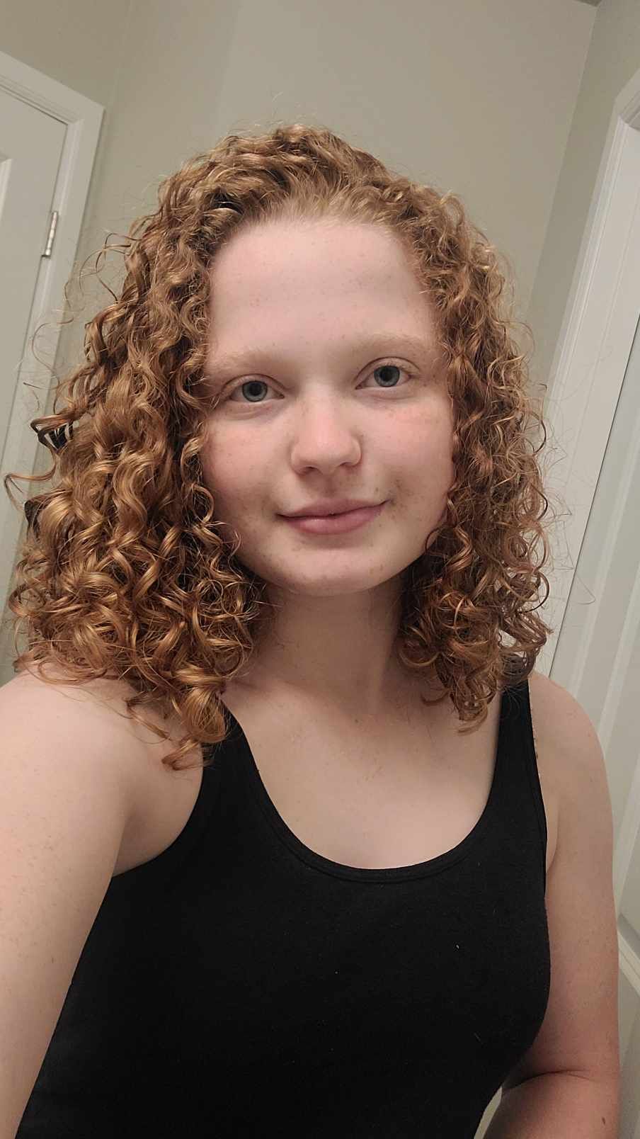 A young woman with red curly hair is taking a selfie in front of a mirror.