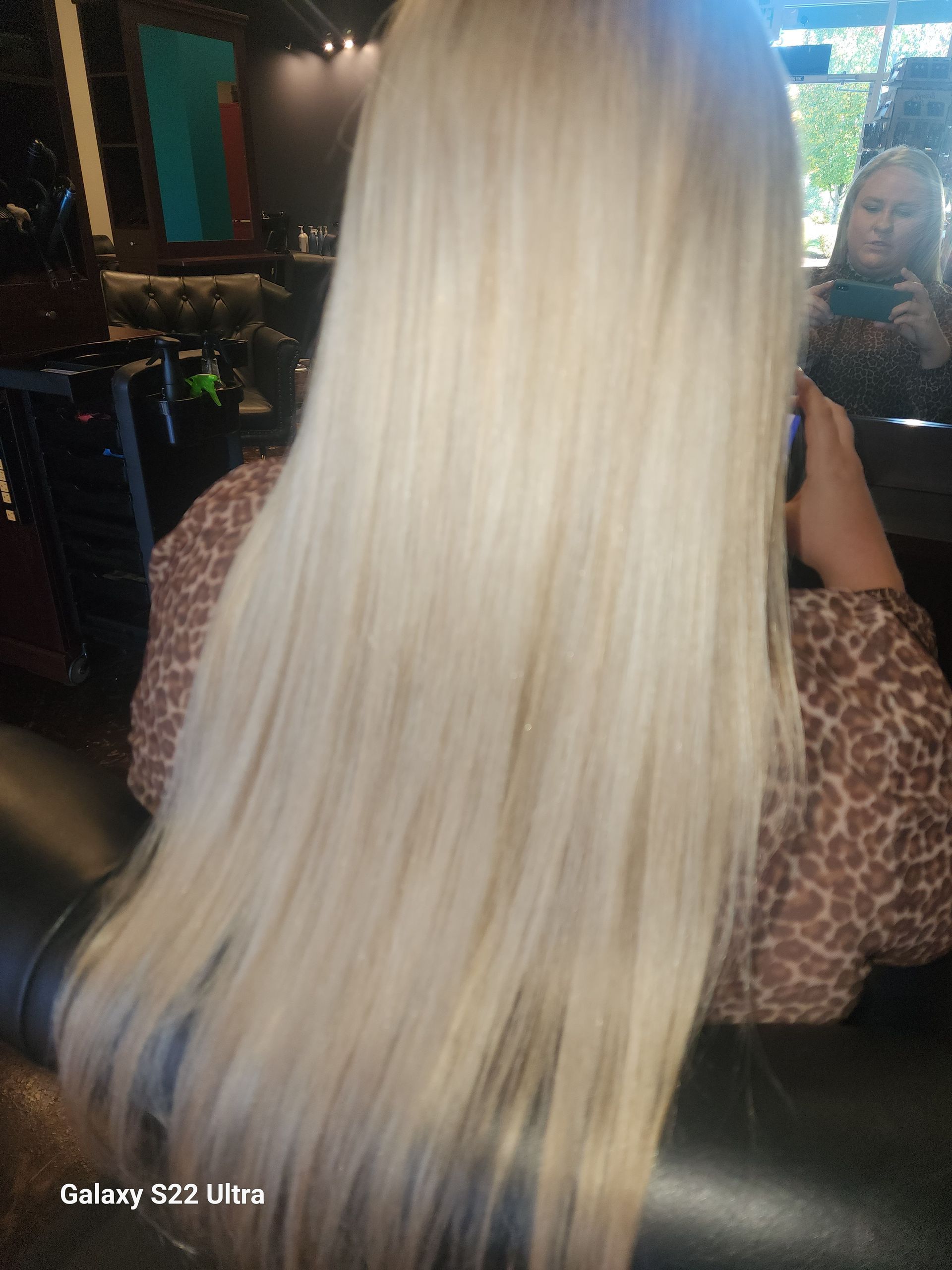 A woman with long blonde hair is sitting in a chair in a salon.