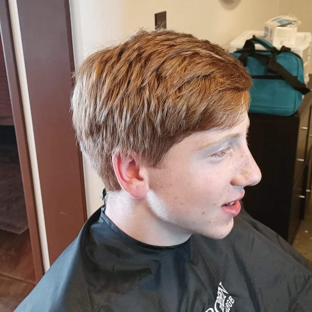 A young man wearing a black cape is getting his hair cut