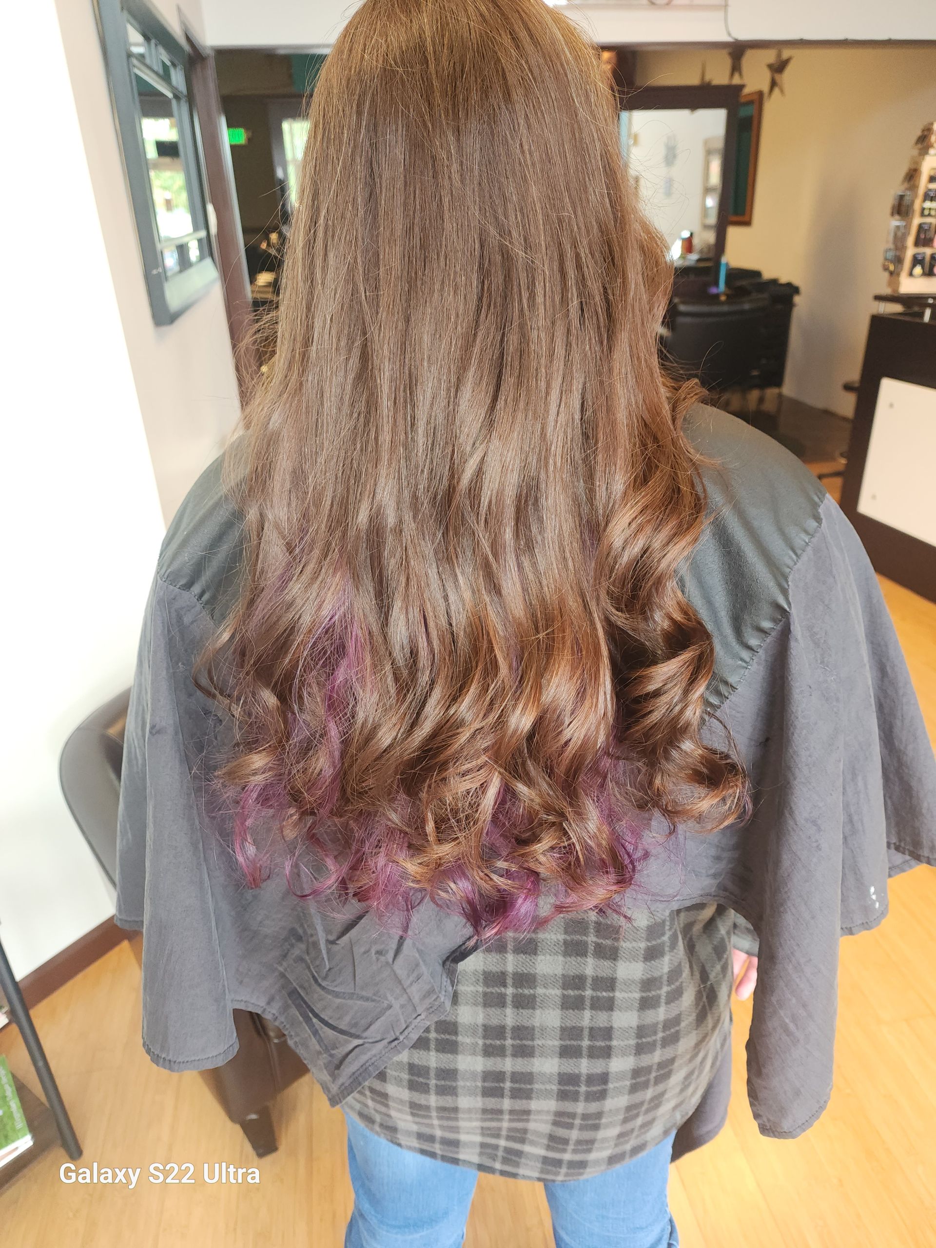 A woman with long brown hair and purple highlights is standing in a salon.