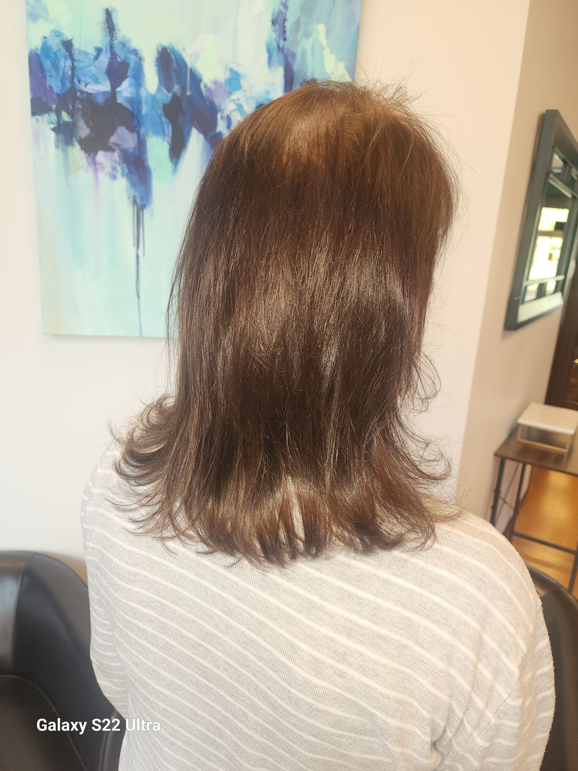 A woman with long hair is sitting in a chair in front of a painting.