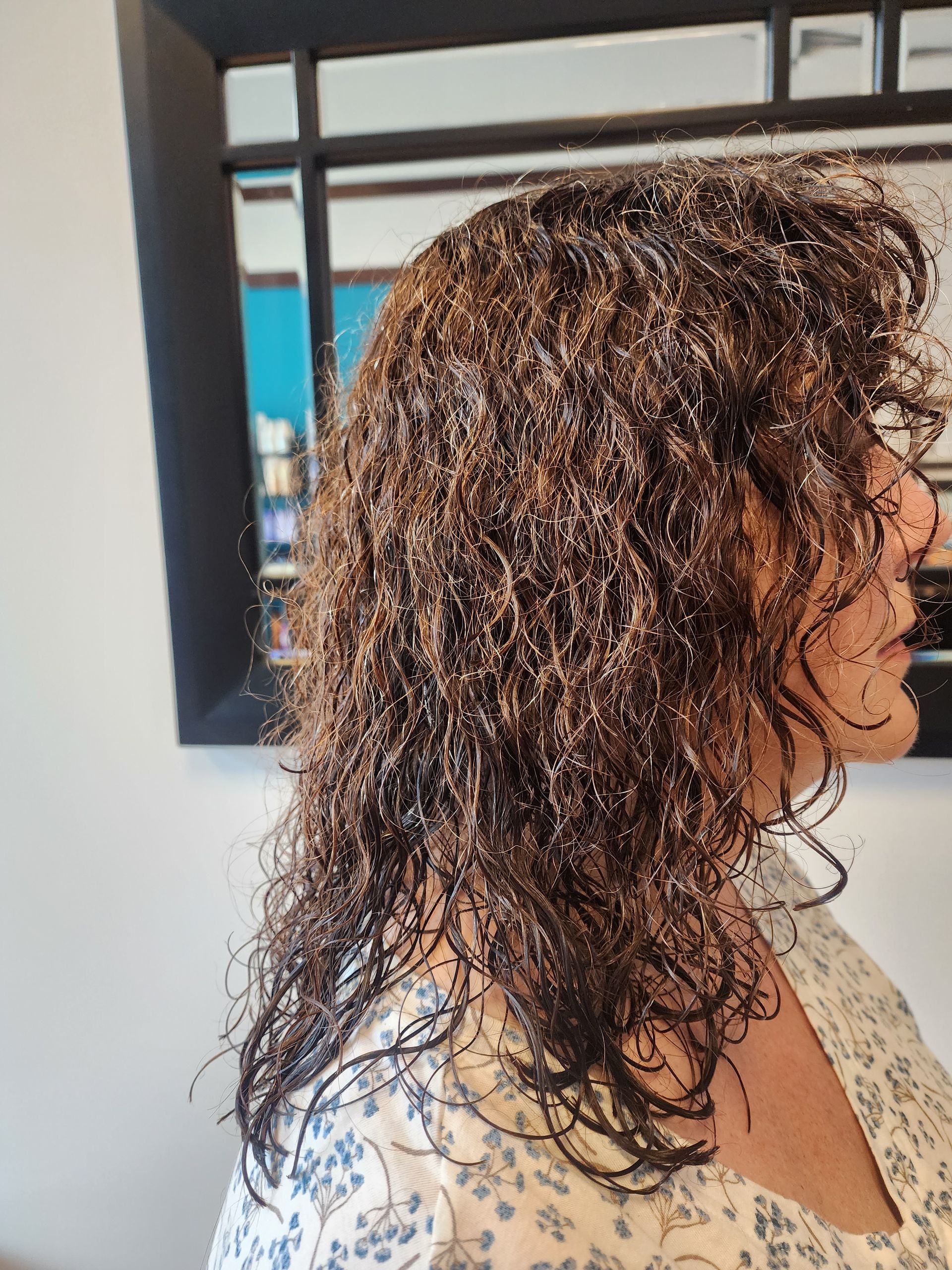 A woman with curly hair is standing in front of a mirror.