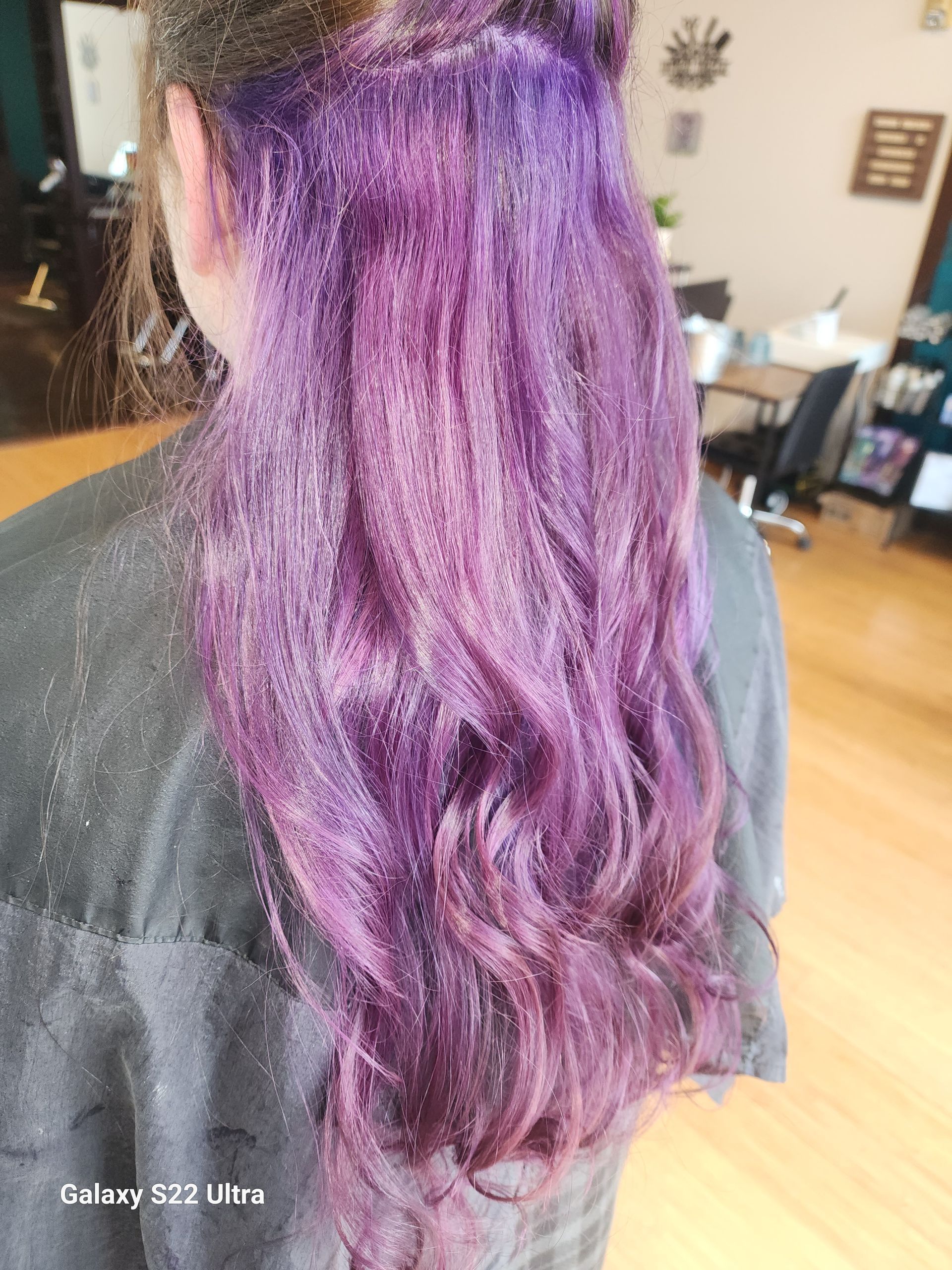 A woman with purple hair is getting her hair dyed in a salon.