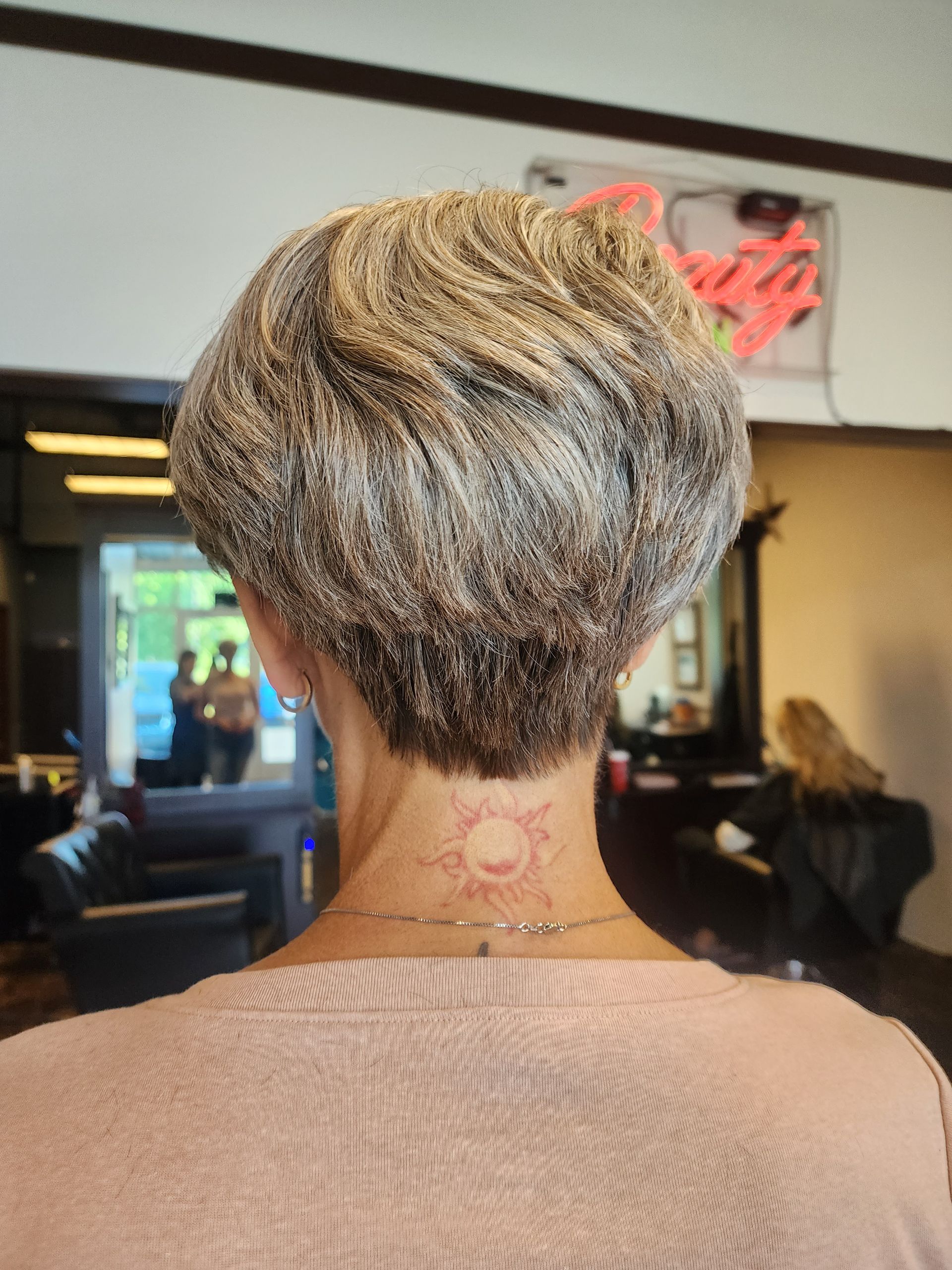 The back of a woman 's head with short hair and a tattoo on her neck.