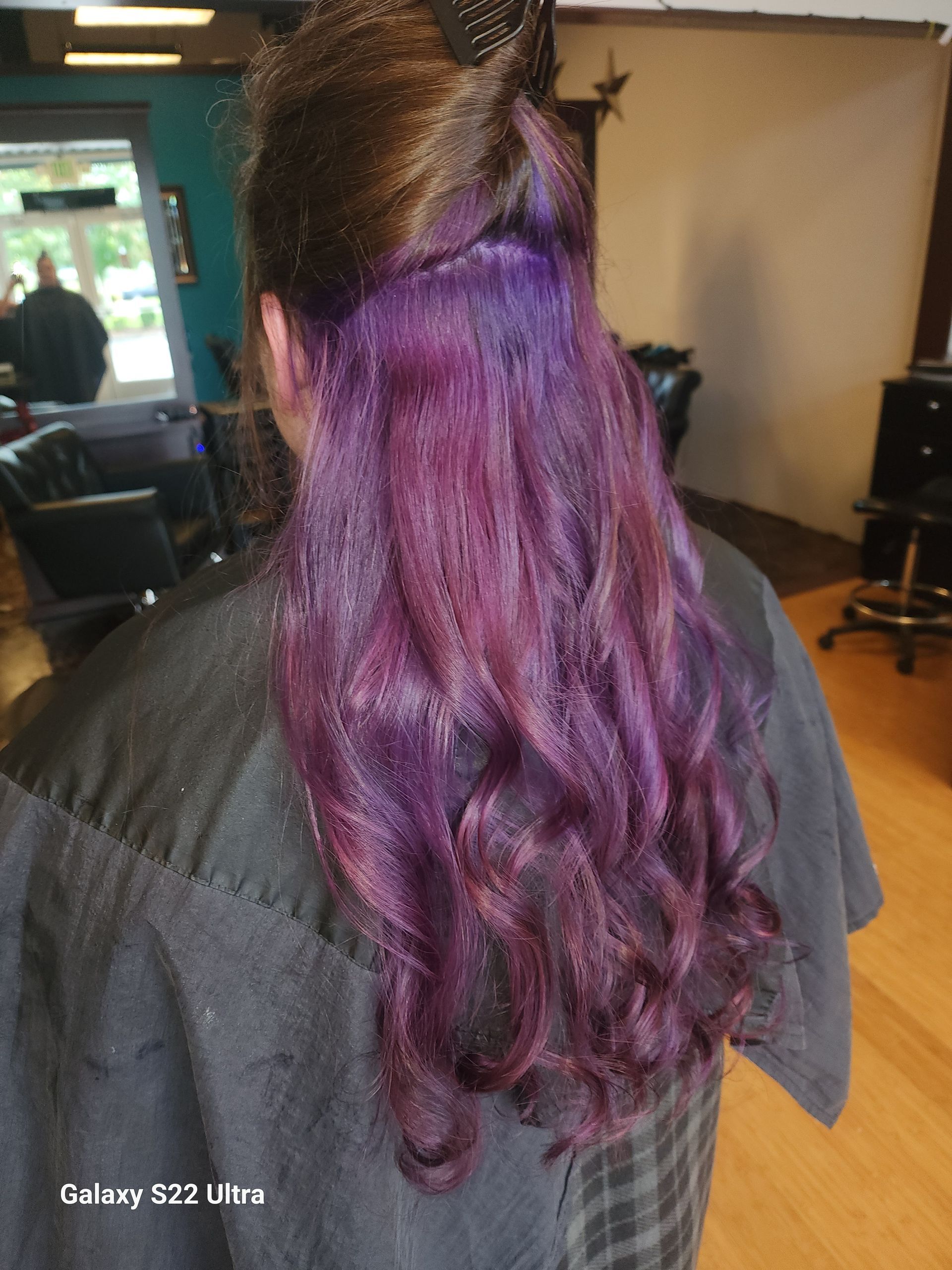 A woman with purple hair is getting her hair dyed in a salon.