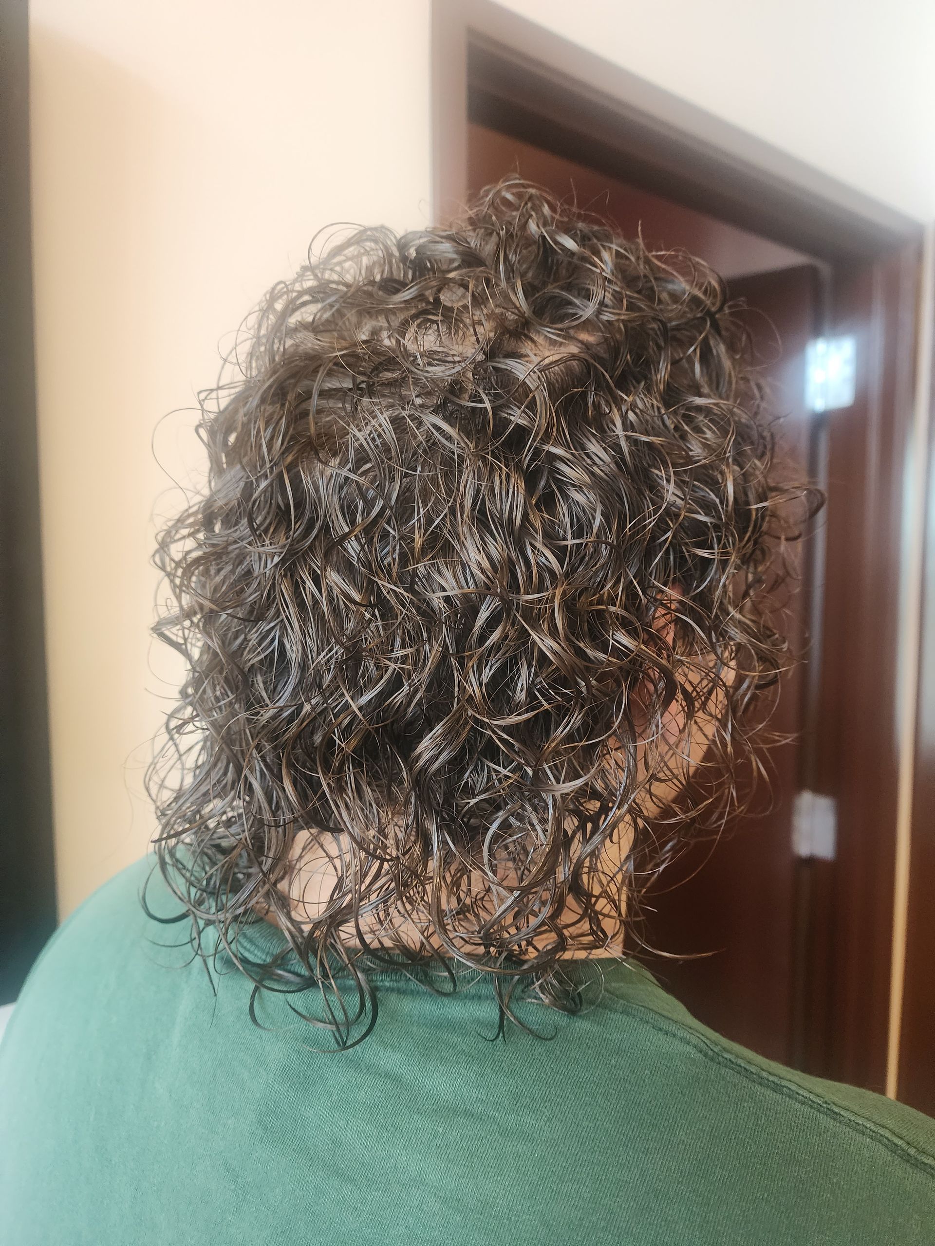 A person with curly hair is wearing a green sweater.