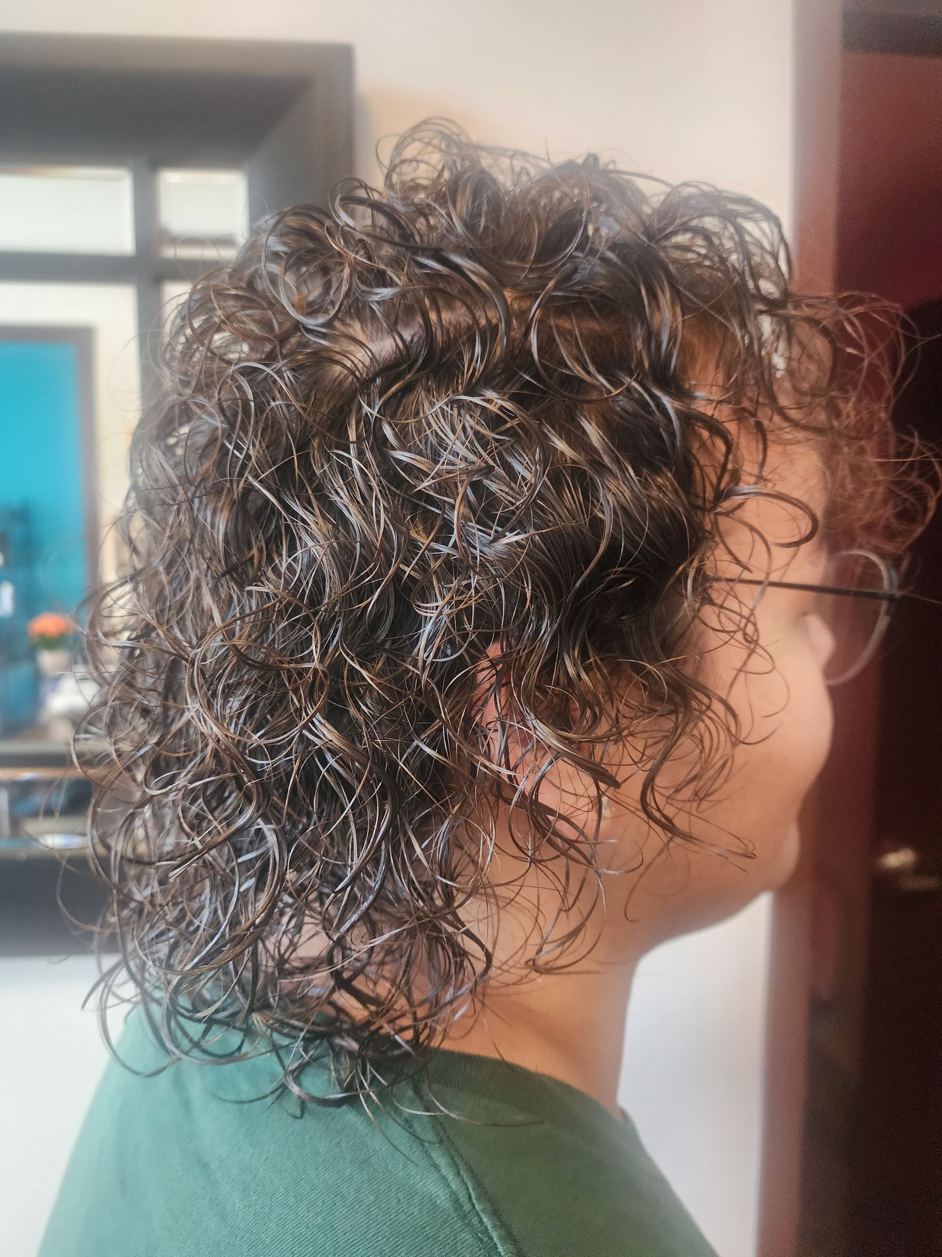 A woman with curly hair is wearing glasses and a green shirt.