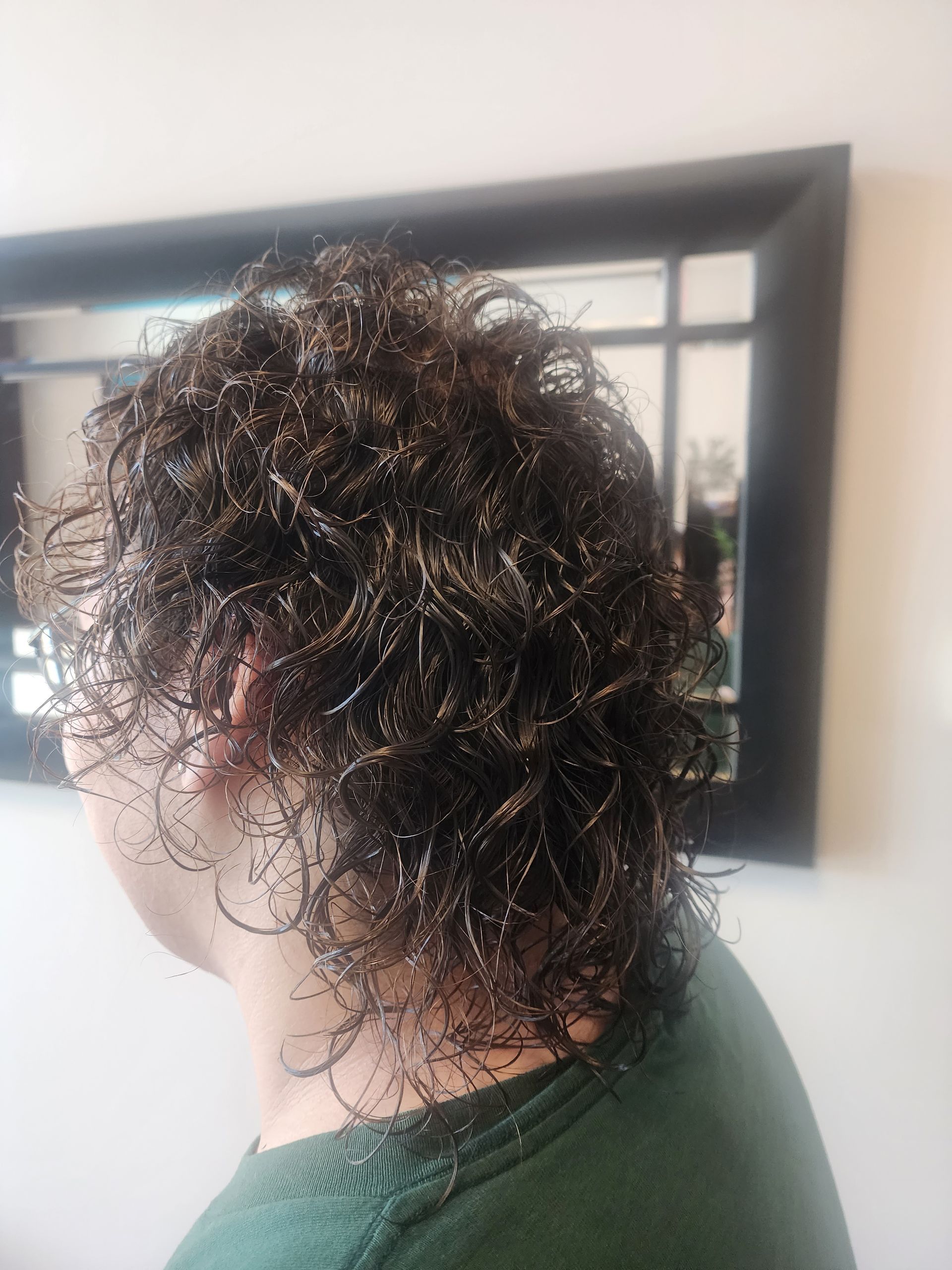 A man with curly hair is standing in front of a mirror.