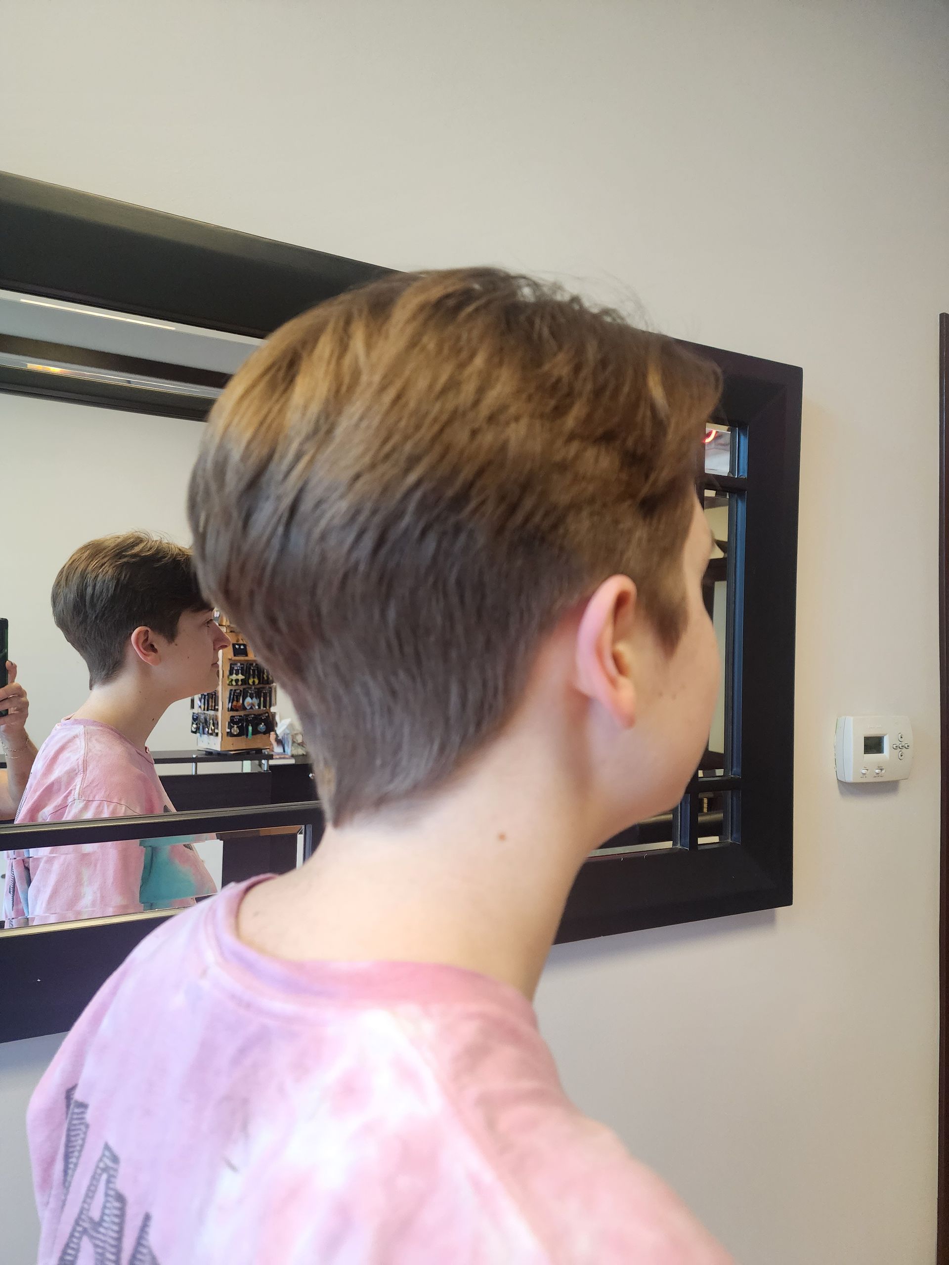 A young boy with short hair is standing in front of a mirror.
