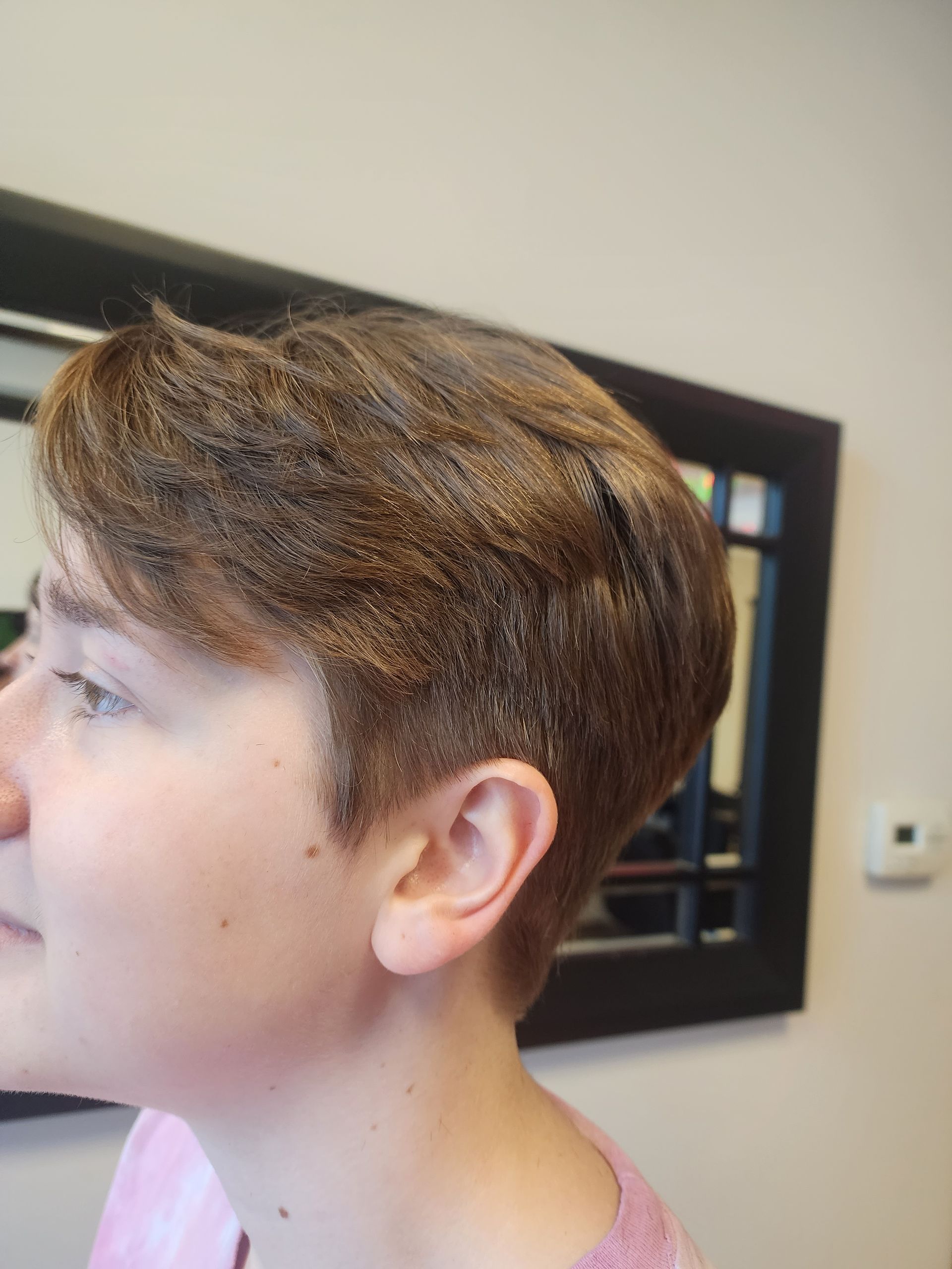 A young boy with short hair is standing in front of a mirror.