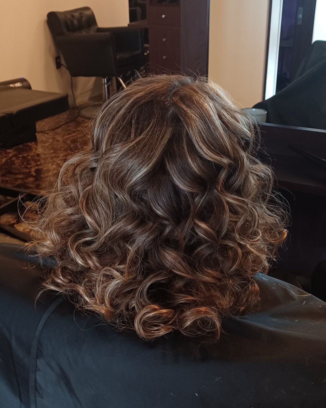 A woman with curly hair is sitting in a chair in a salon.