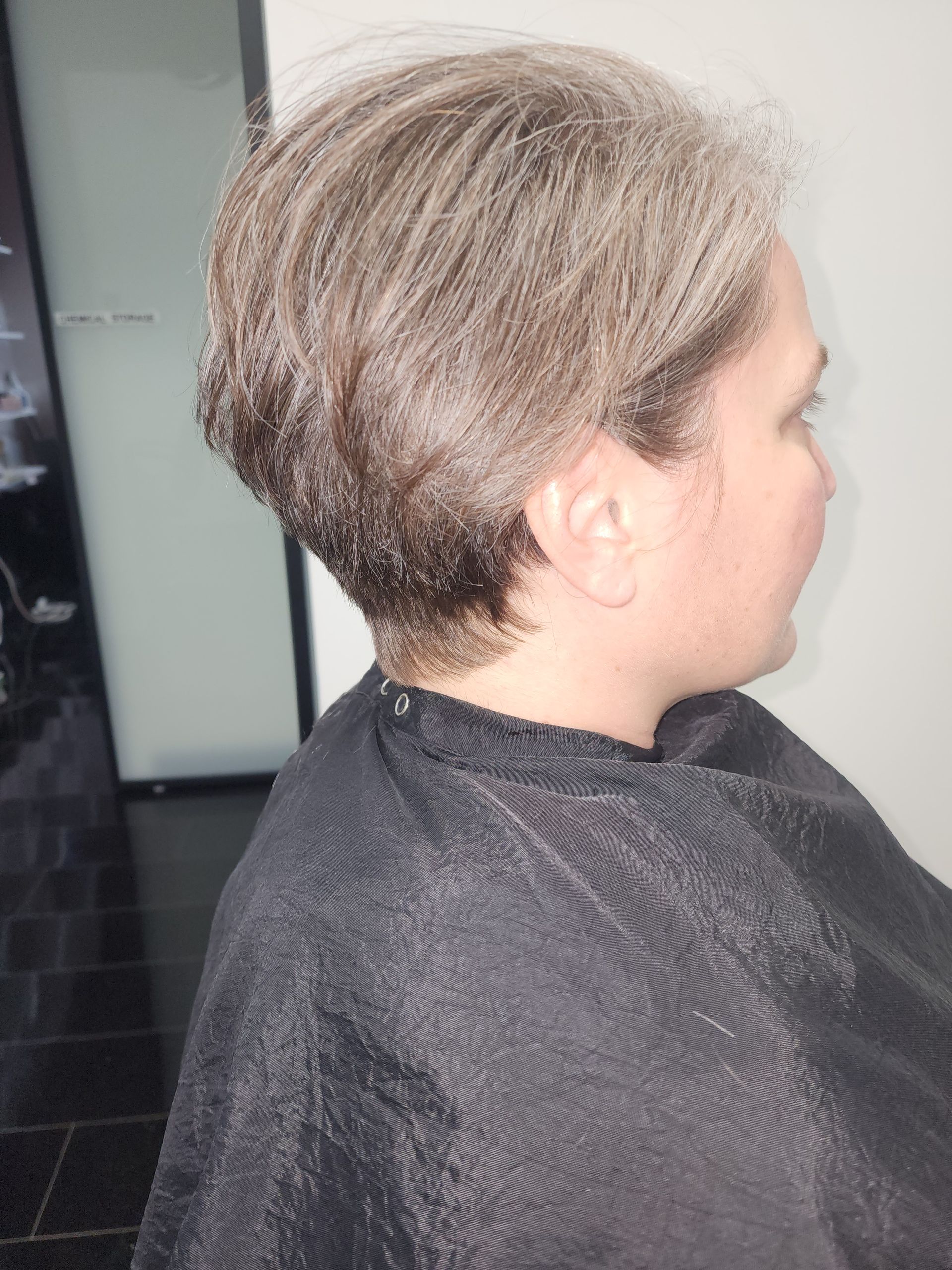 A woman in a black cape is getting her hair cut.