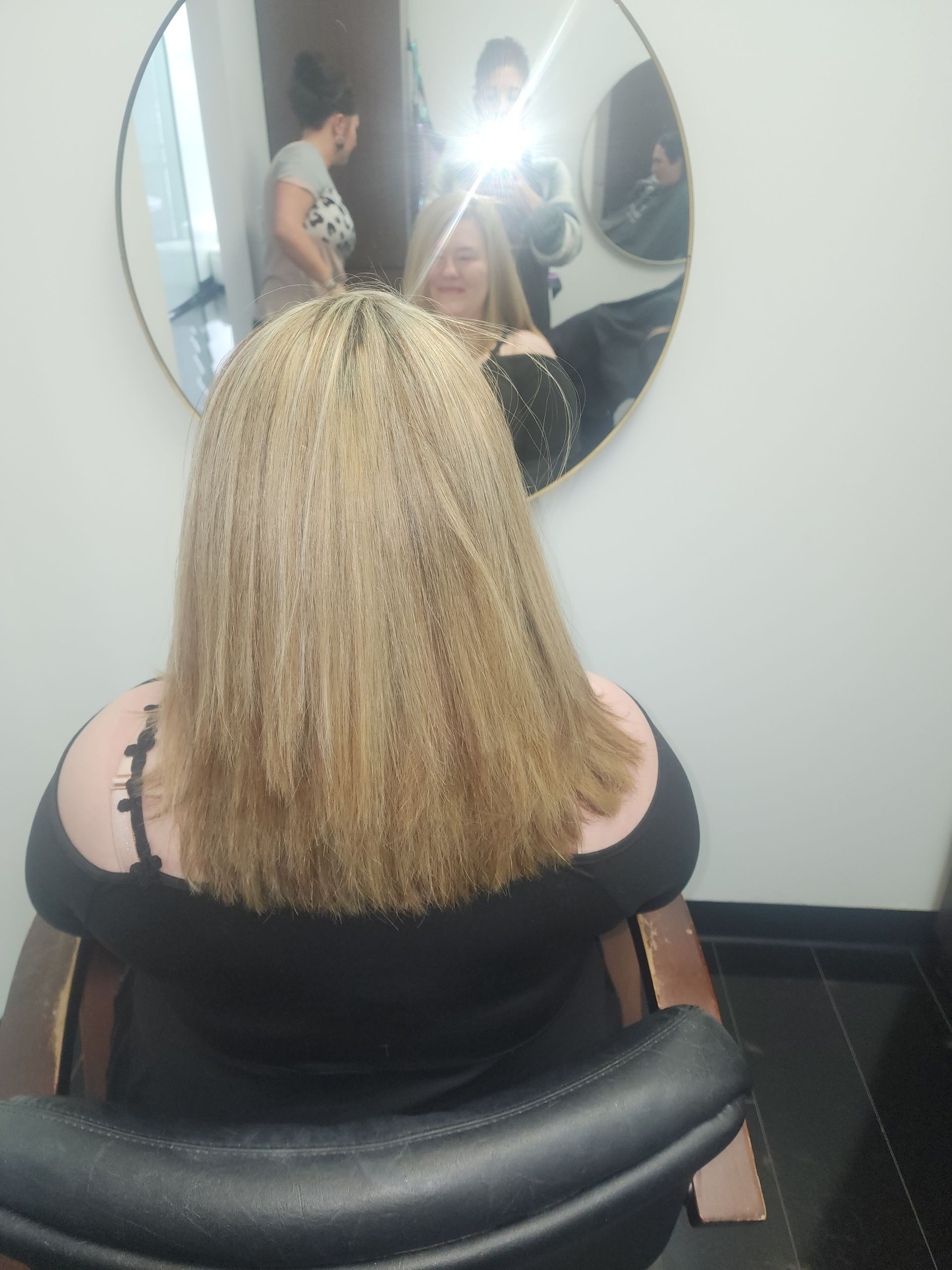 A woman is sitting in a chair looking at her hair in a mirror.