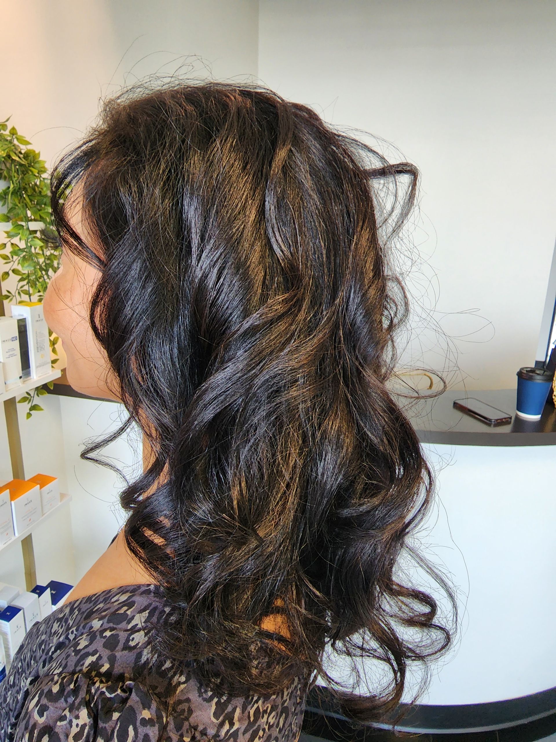 A woman with long dark hair is standing in a salon.