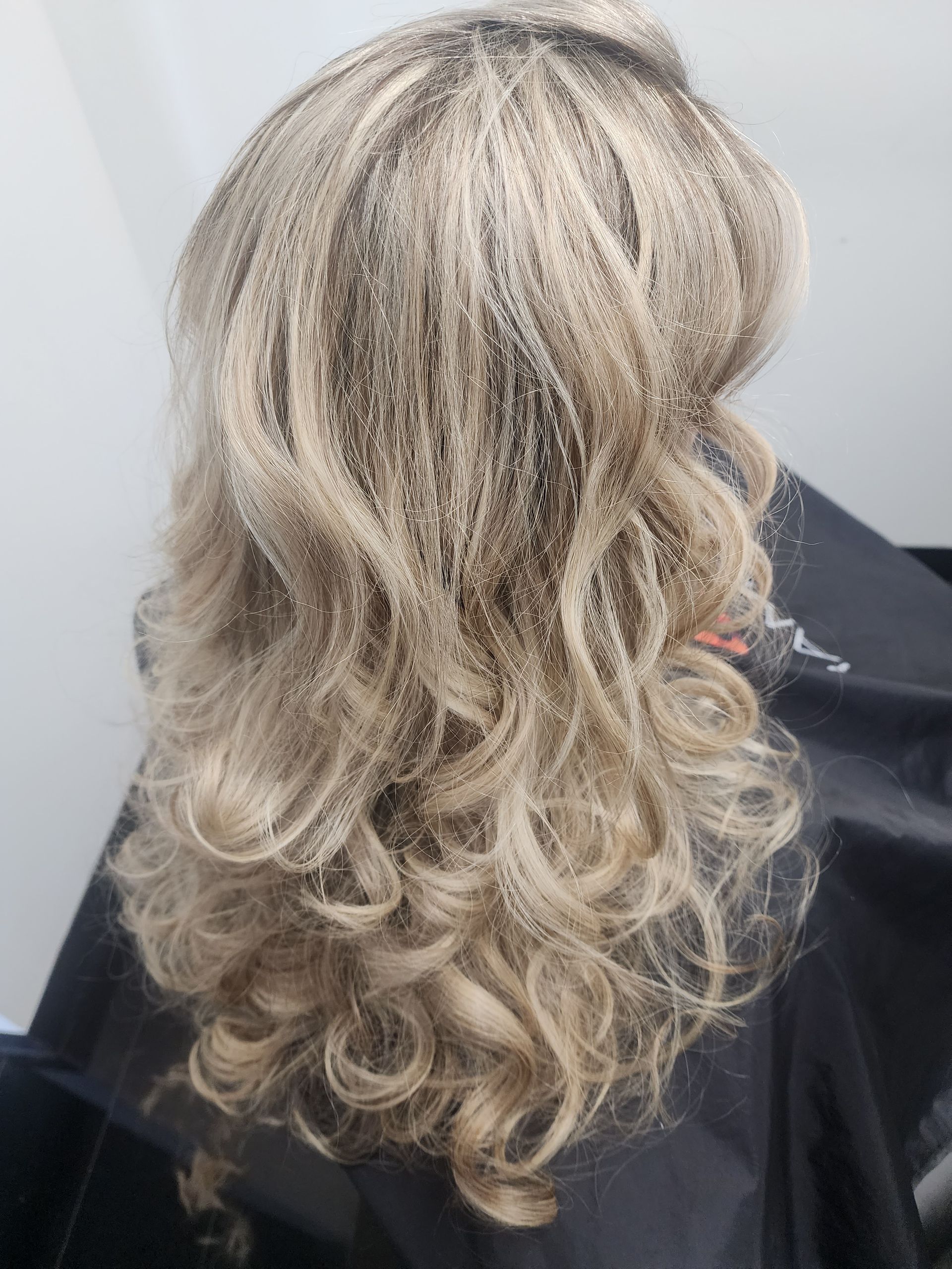 A woman with long blonde curly hair is sitting in a chair.